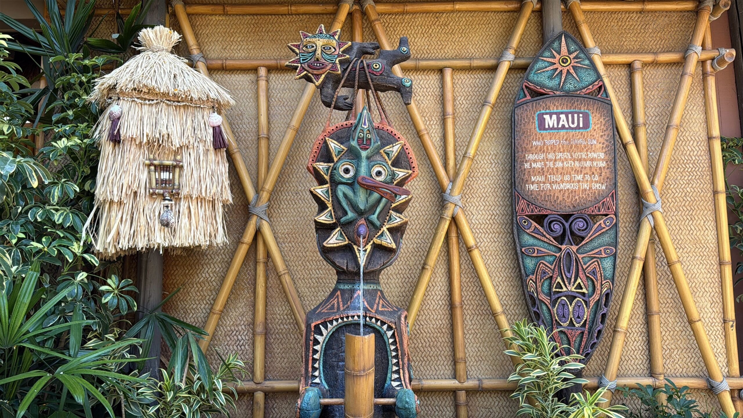 Tiki statues, a straw hut, and an Enchanted Tiki Room sign pop against bamboo walls and lush tropical plants.