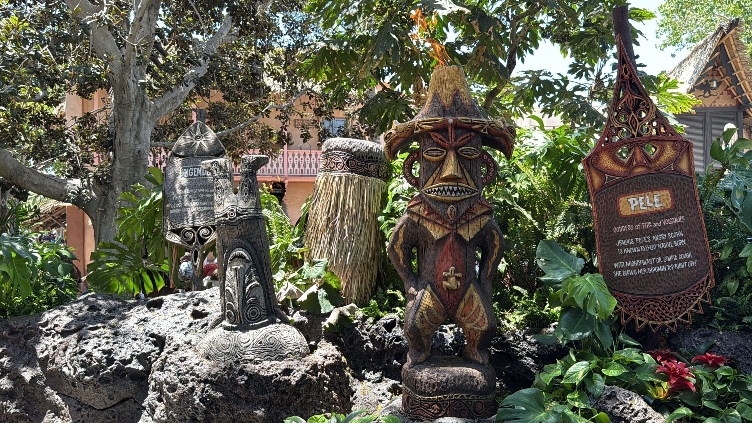 Four colorful tiki statues with intricate designs evoke the enchanted tiki room in a lush, tropical Disneyland setting.