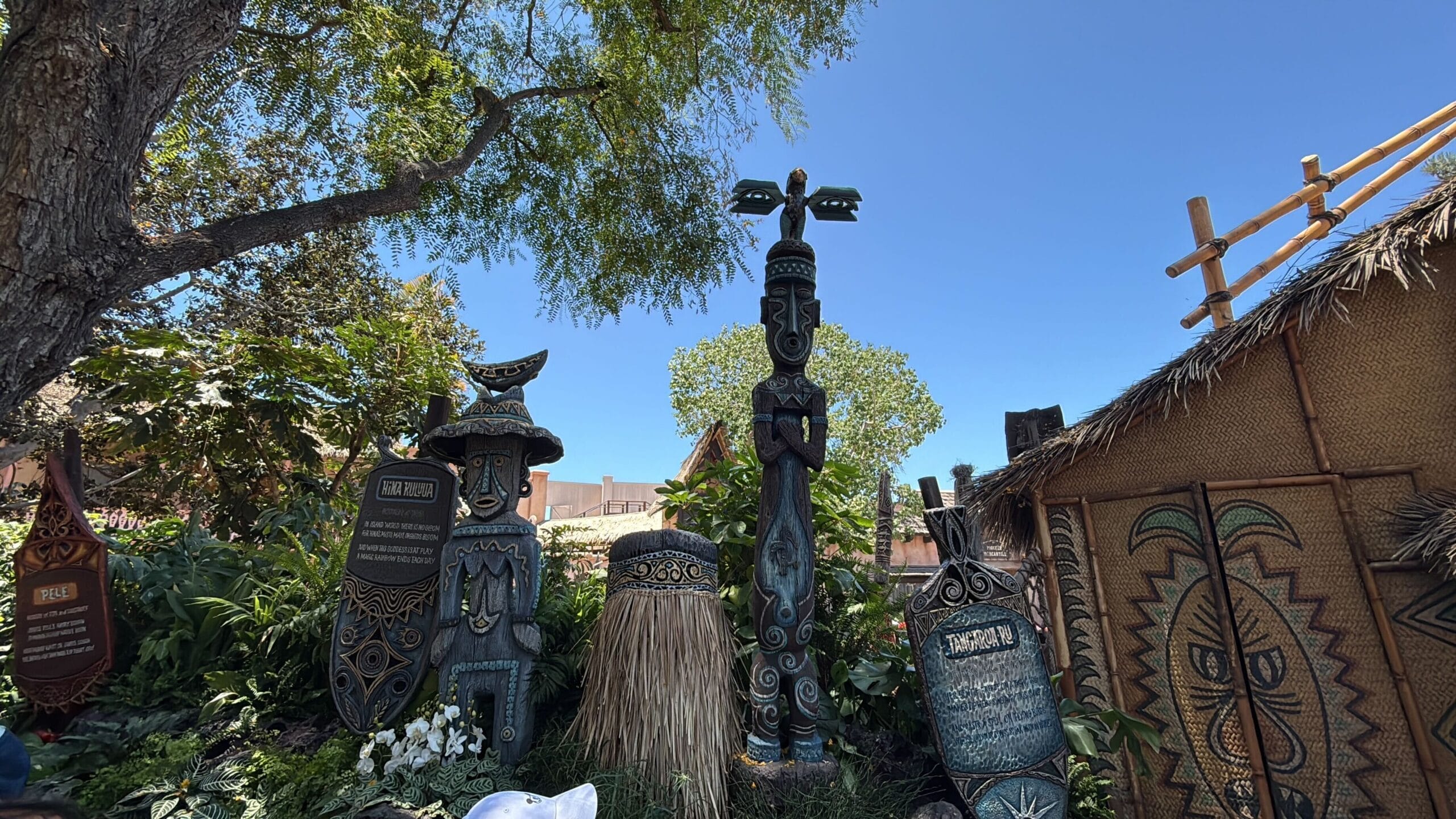 Colorful Polynesian statues and tiki carvings by lush plants at Disneyland’s Enchanted Tiki Room reopening.
