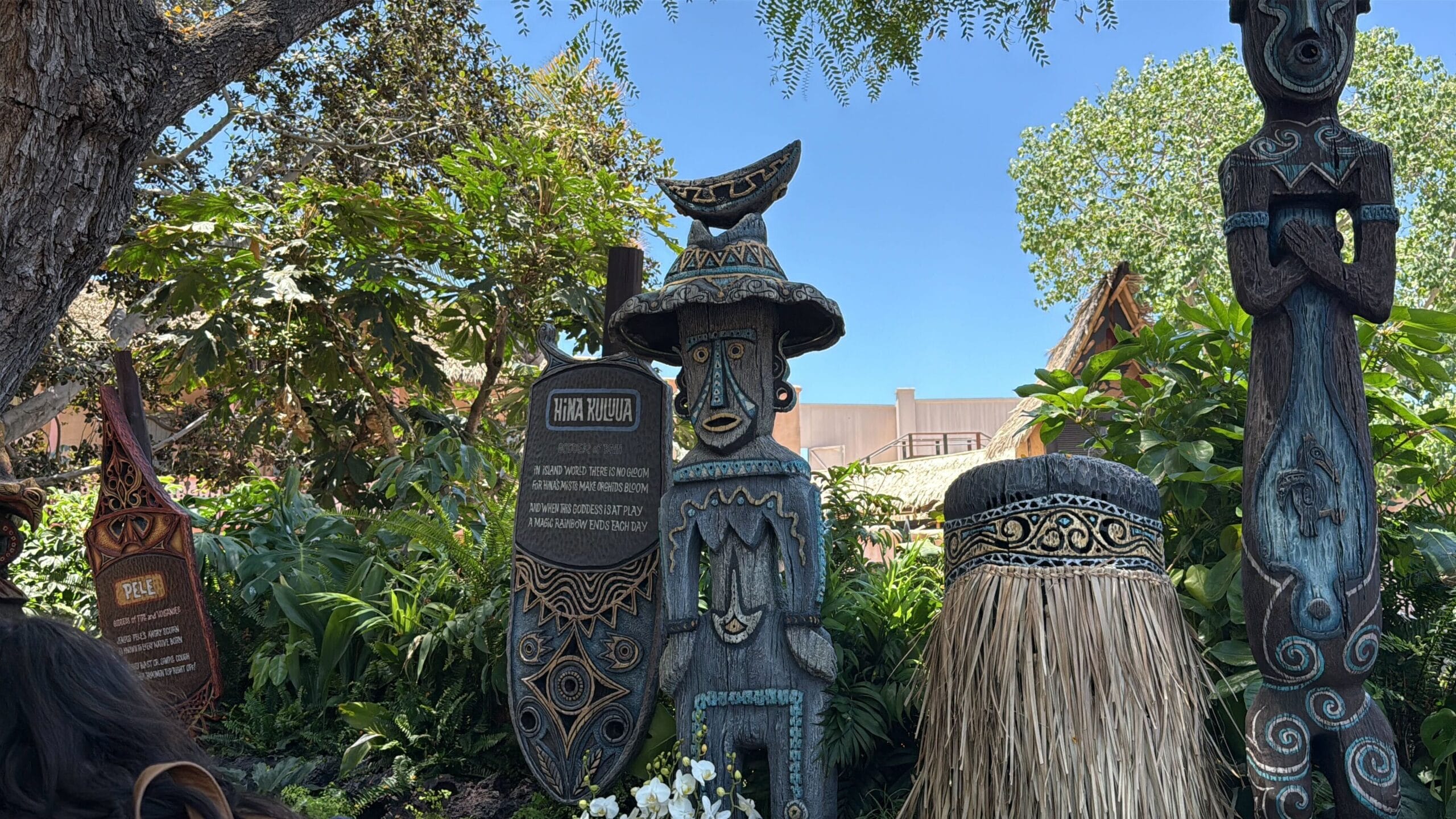 Three Polynesian-style tiki statues welcome guests to the Disneyland Enchanted Tiki Room, surrounded by lush greenery.