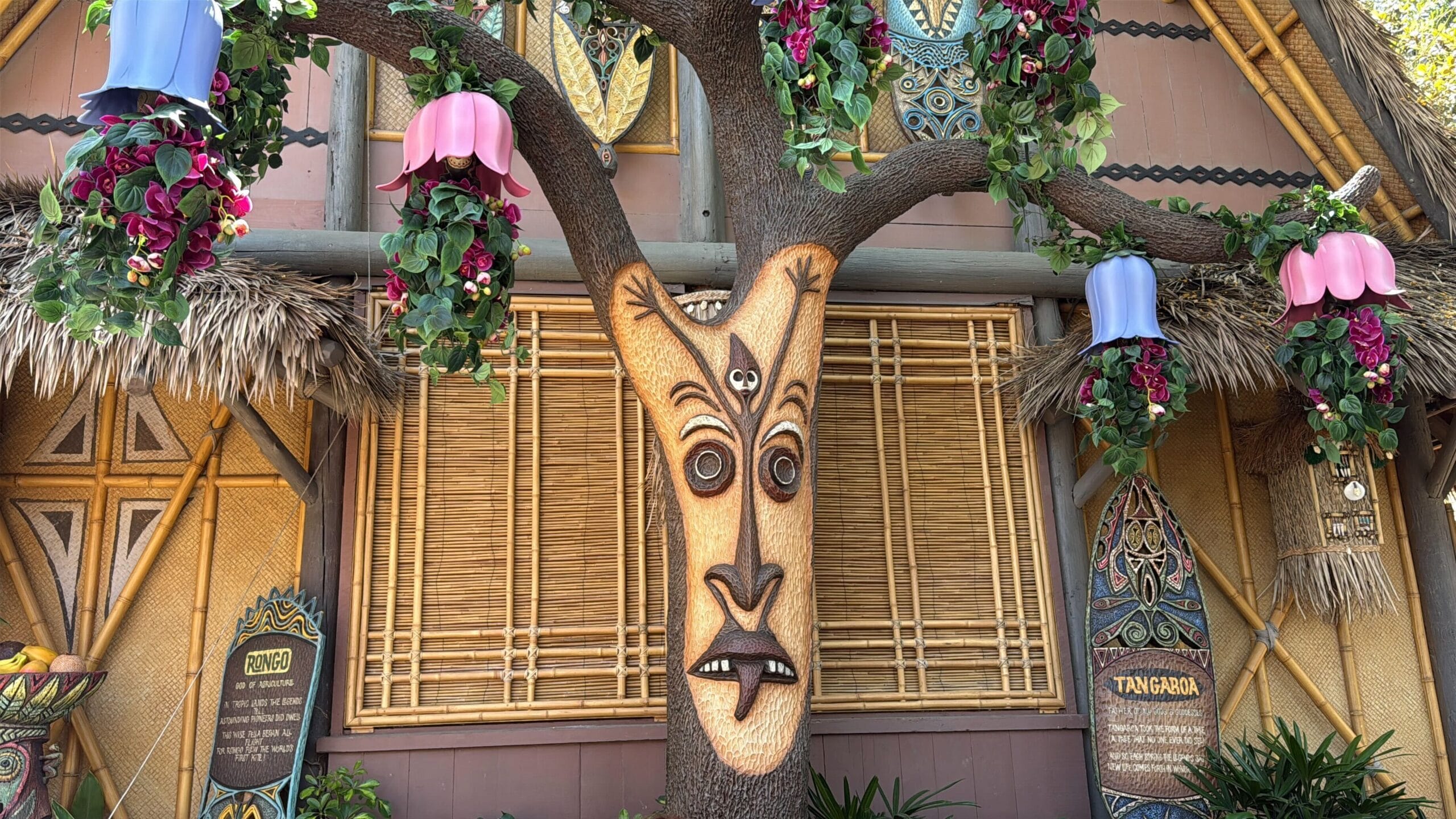 A tree with a carved face and flowers hangs lanterns outside the enchanted tiki room at Disneyland, ready for its reopening.