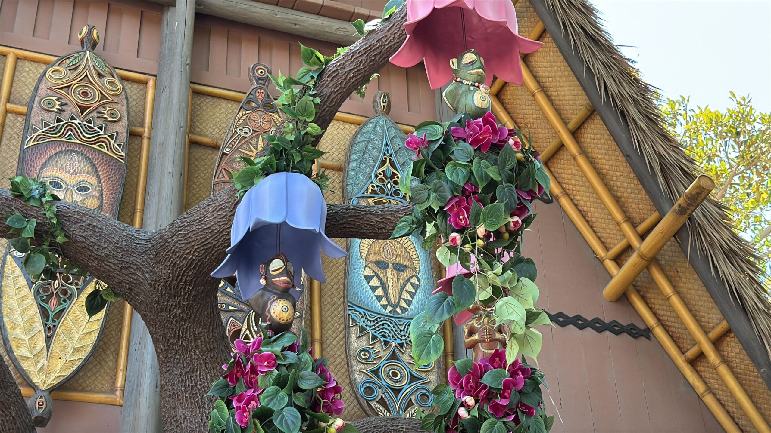 Decorative poles with flowers and masks by tribal carvings, evoking Disneyland’s Enchanted Tiki Room reopening magic.