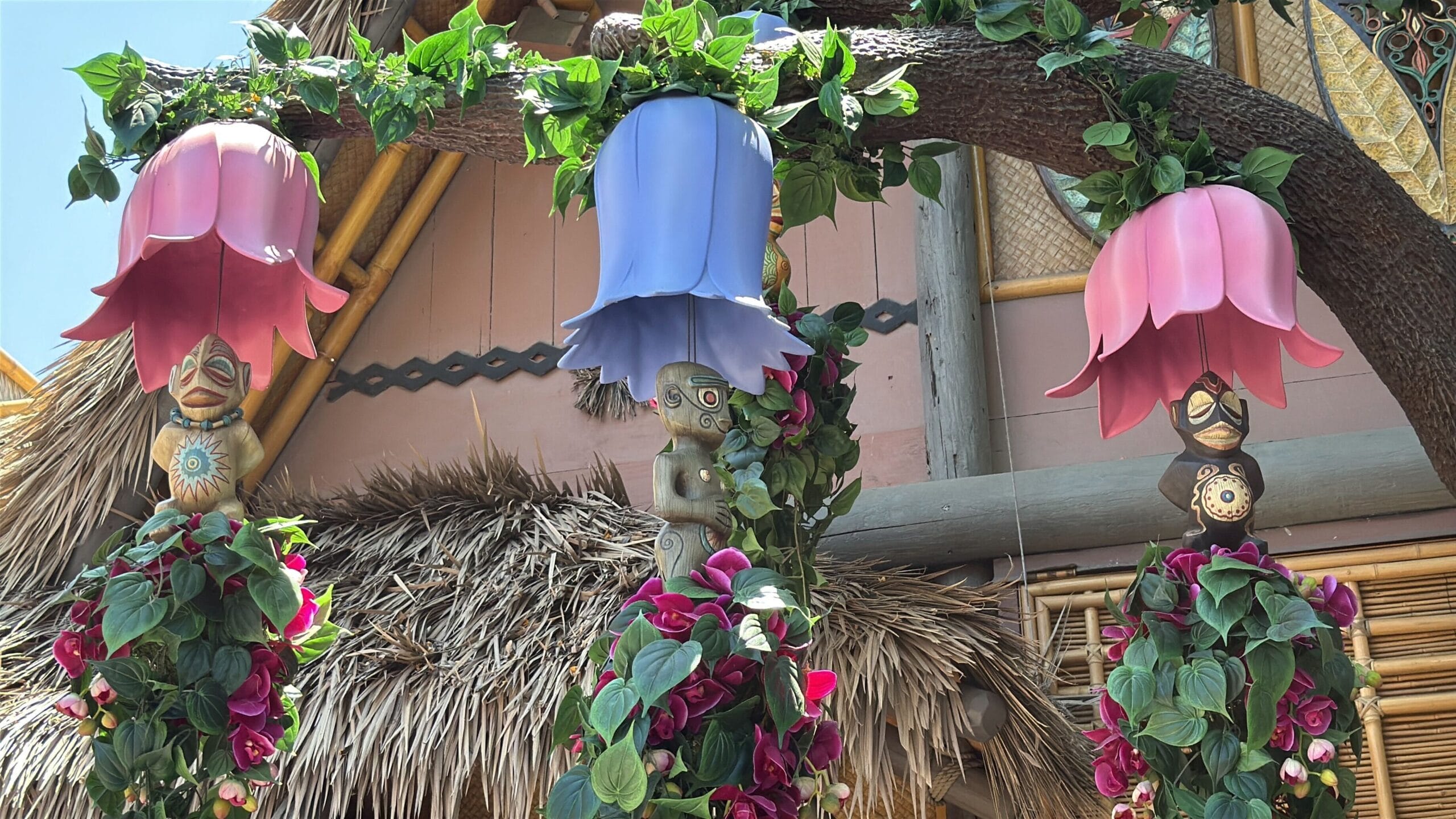 Three colorful tiki lanterns with leafy vines hang from a tree in an enchanted tiki room at Disneyland.