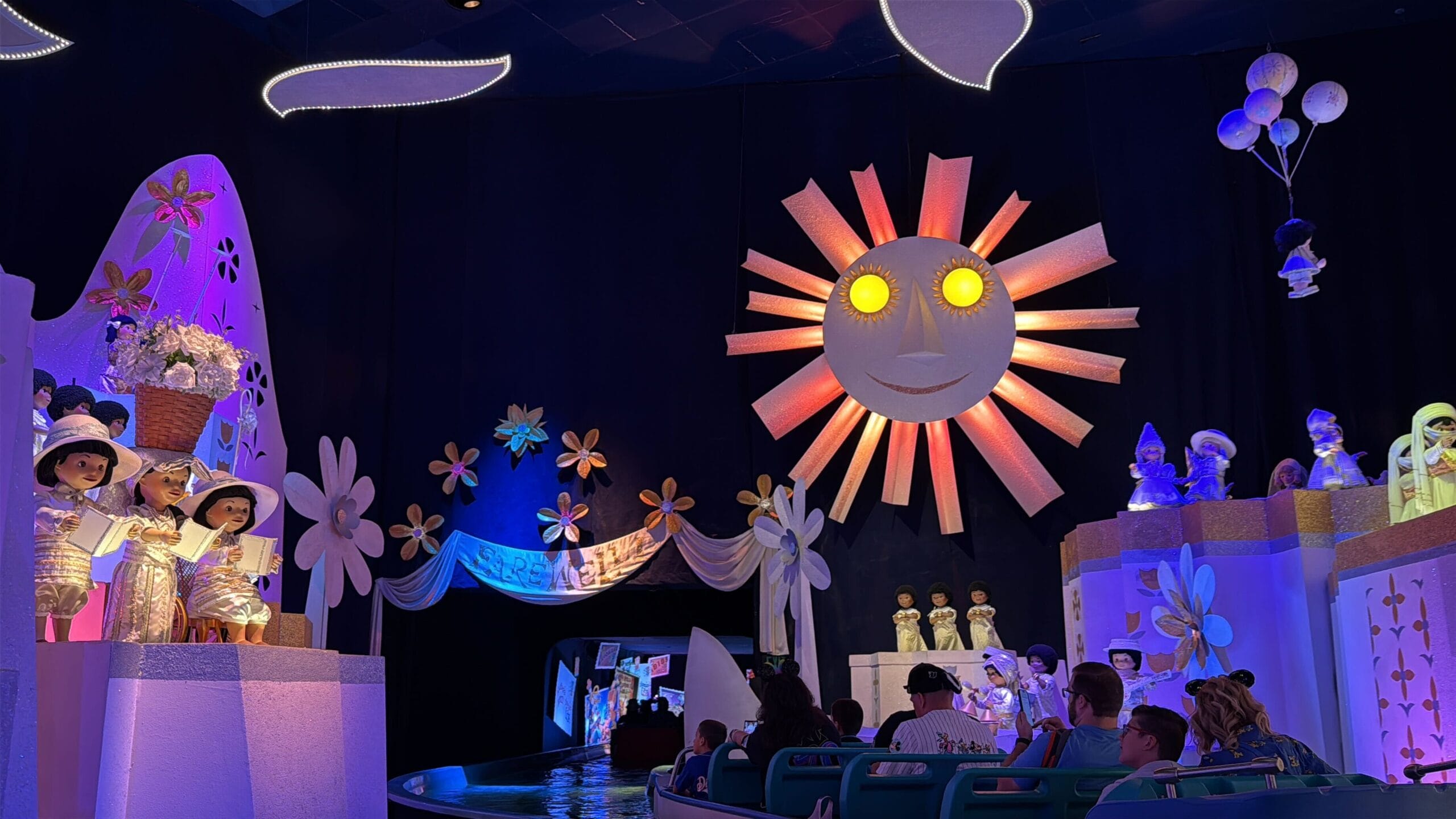 Colorful indoor boat ride at Disneyland with glowing sun, animated dolls, flowers, and whimsical "it's a small world" joy.