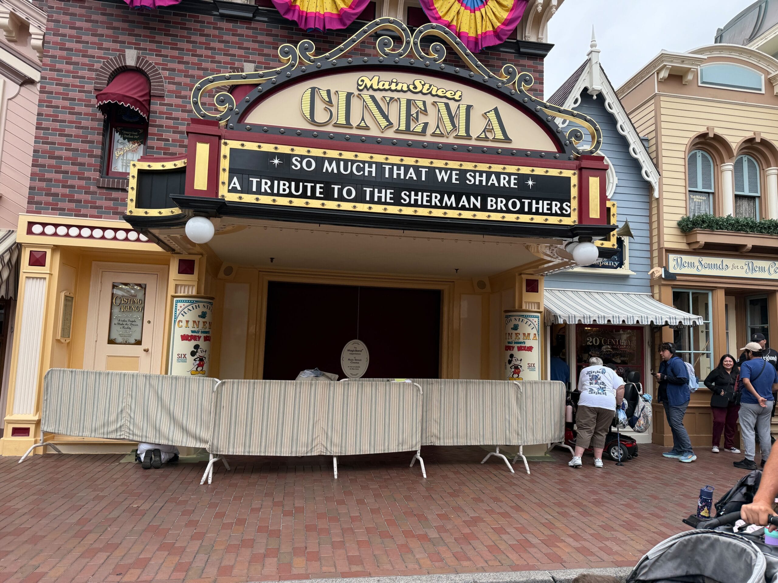 Main Street Cinema with sign reading "Tribute to the Sherman Brothers," barriers in front, and people walking by.