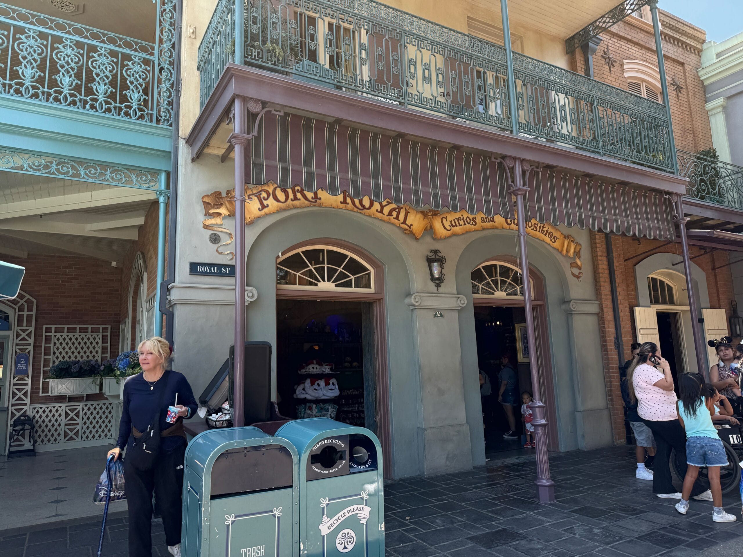 A woman stands by trash cans near the Port Royal shop entrance, steps from the Haunted Mansion in Disneyland’s New Orleans Square.