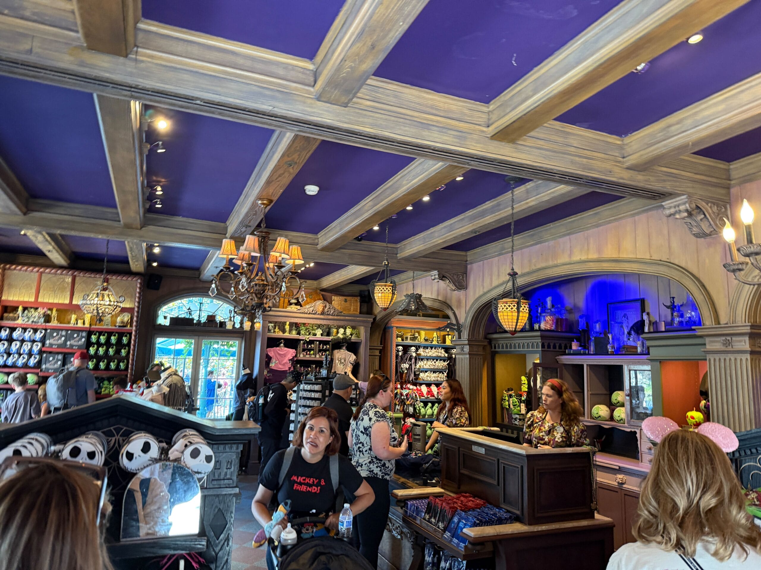 Crowded Haunted Mansion Store with purple ceiling, chandeliers, and shelves stocked with Nightmare Before Christmas merchandise.