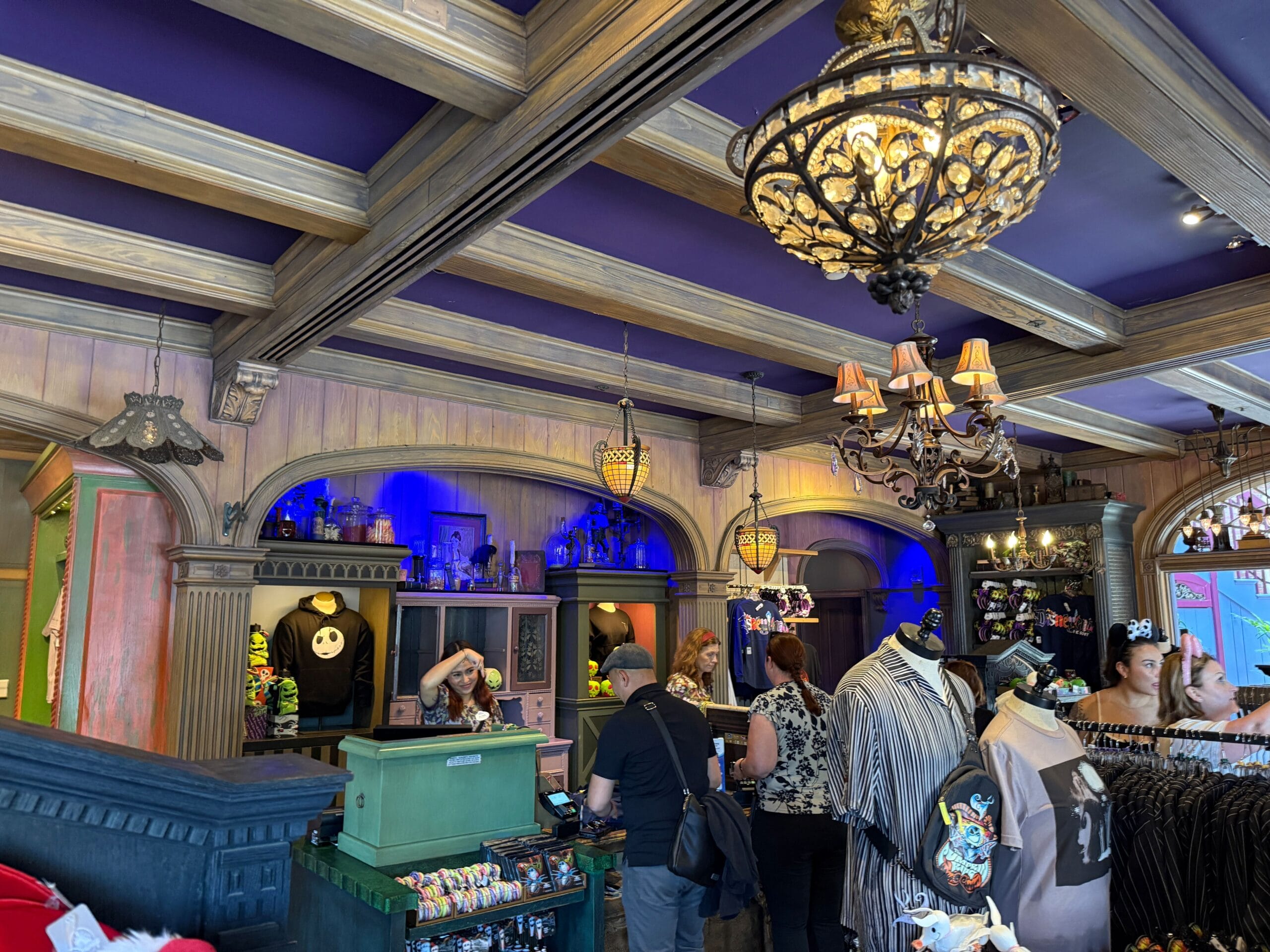 People shop in a Haunted Mansion-themed store with gothic decor, chandeliers, and unique Disneyland merchandise on display.