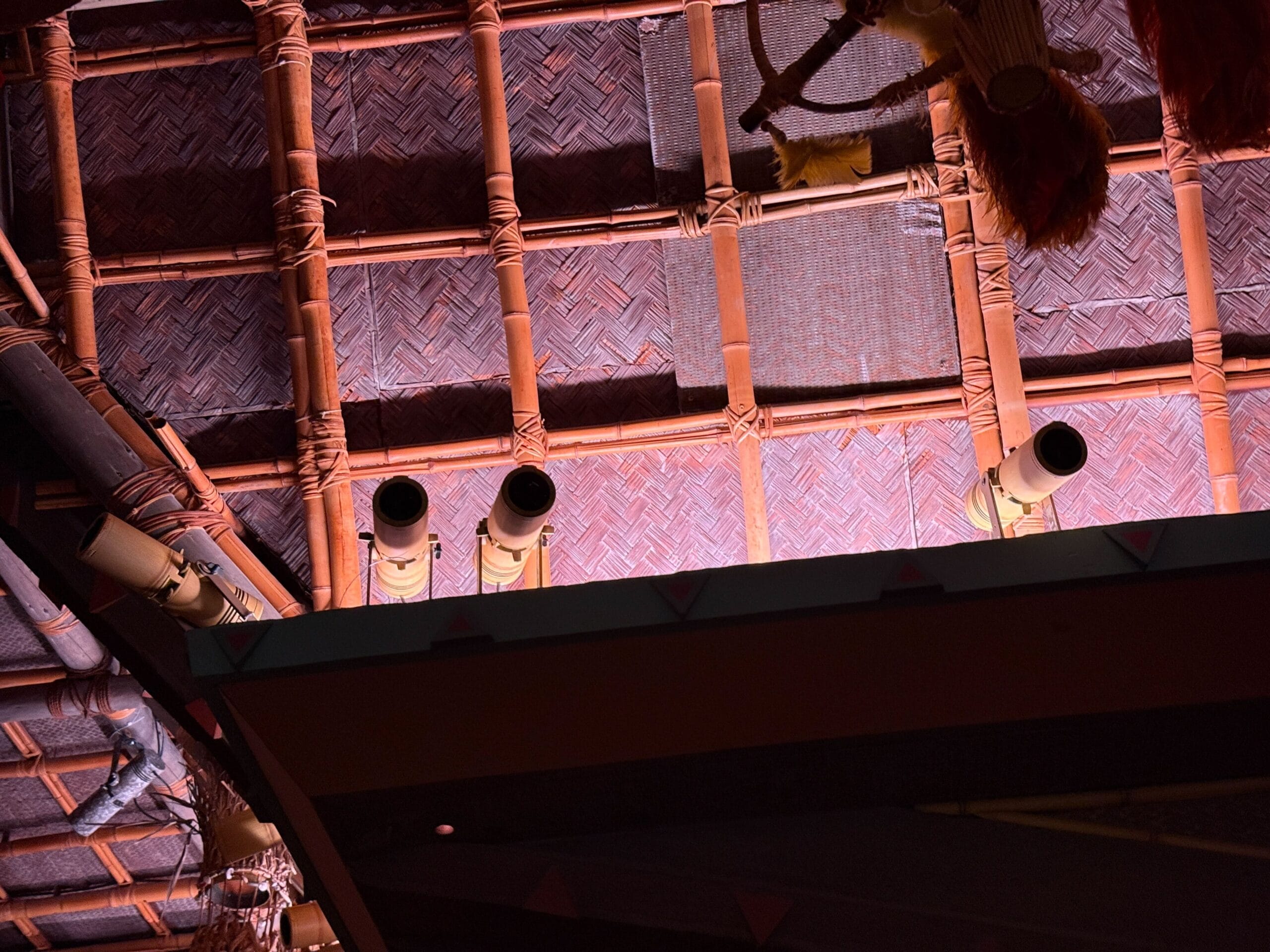 Bamboo pipes and woven panels on a ceiling, glowing warmly—like the enchanted tiki room reopening at Disneyland.