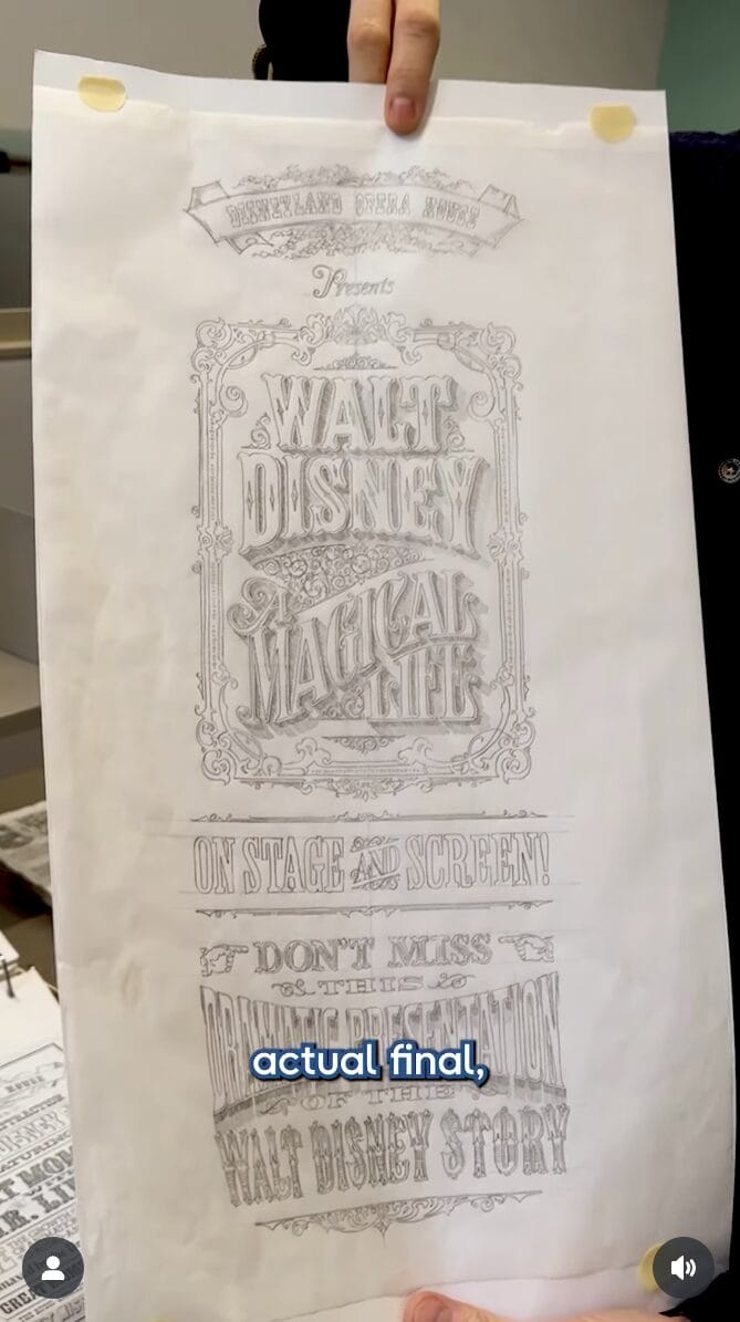 A person holds up an ornate Walt Disney Attraction Poster reading "Magical Life" in detailed hand-drawn lettering.
