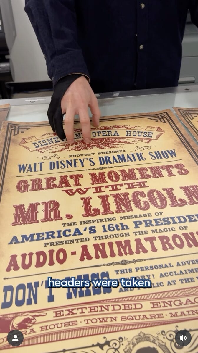 A person in gloves touches a vintage Walt Disney Attraction Poster for the Mr. Lincoln show on a table.
