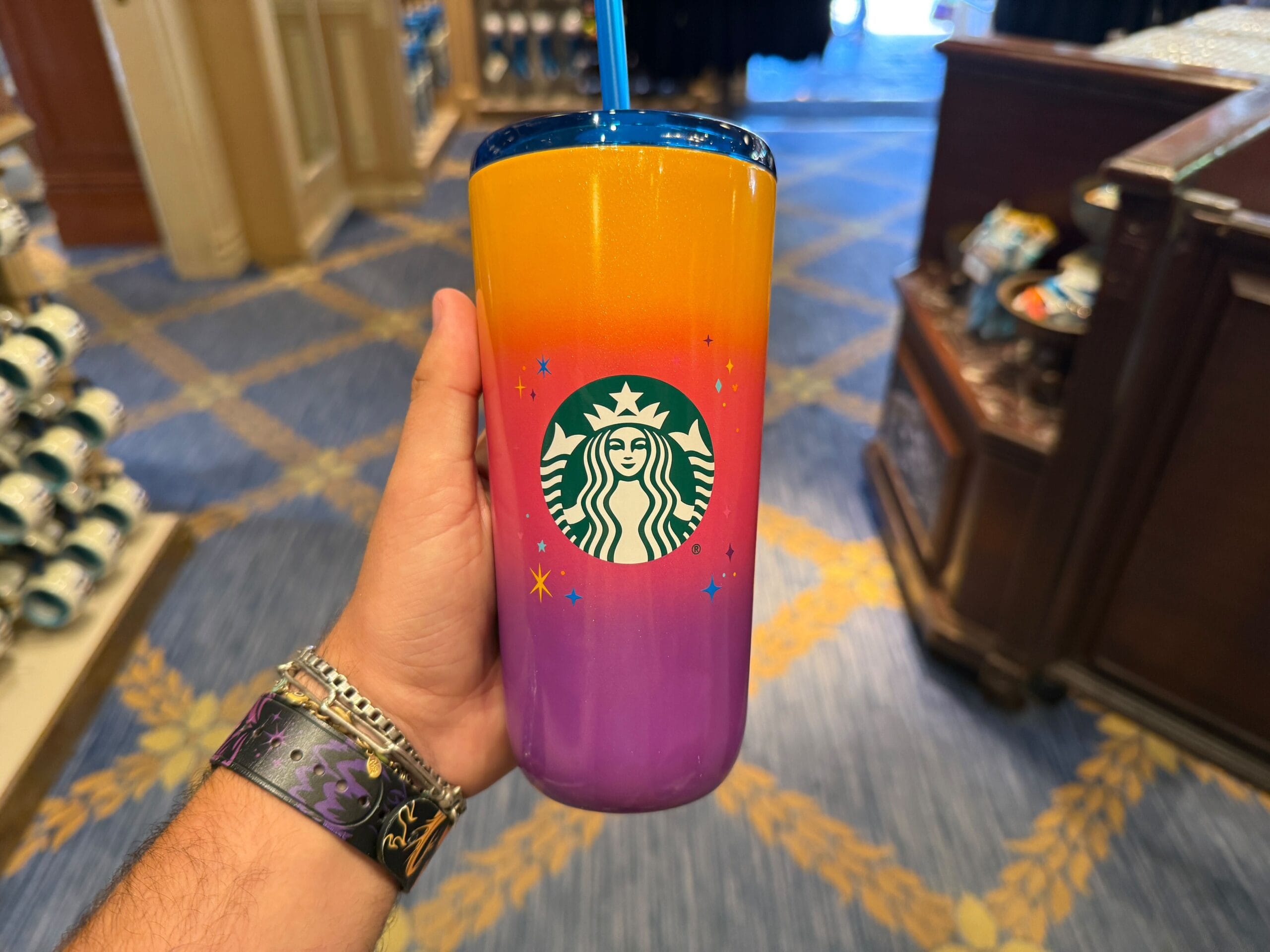 A hand holds a colorful Starbucks tumbler from the Celebrate Happy Collection, with an orange-to-purple gradient and star designs.