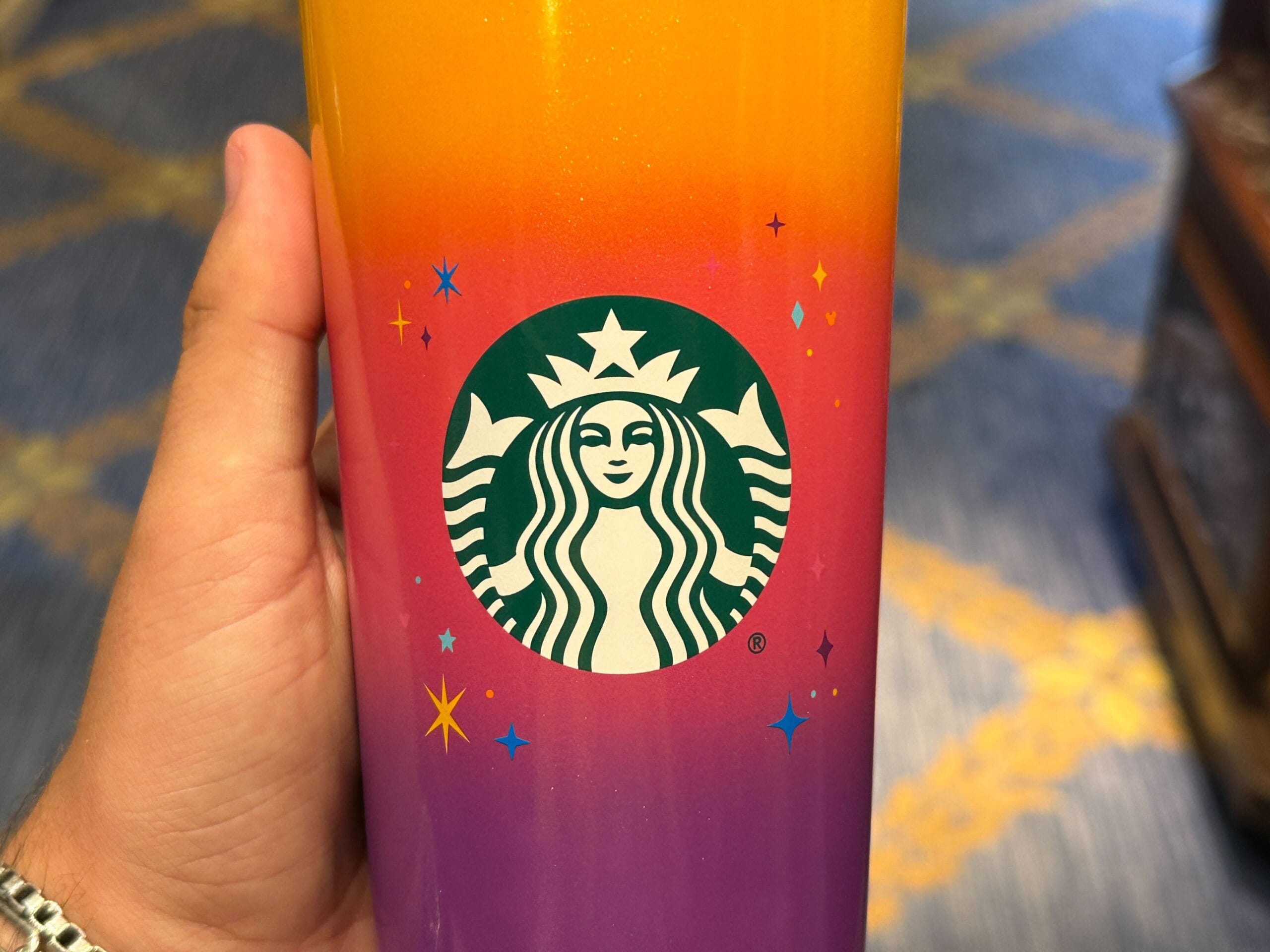 A hand holds a colorful Starbucks cup from the Celebrate Happy Collection, featuring a gradient and small star designs.