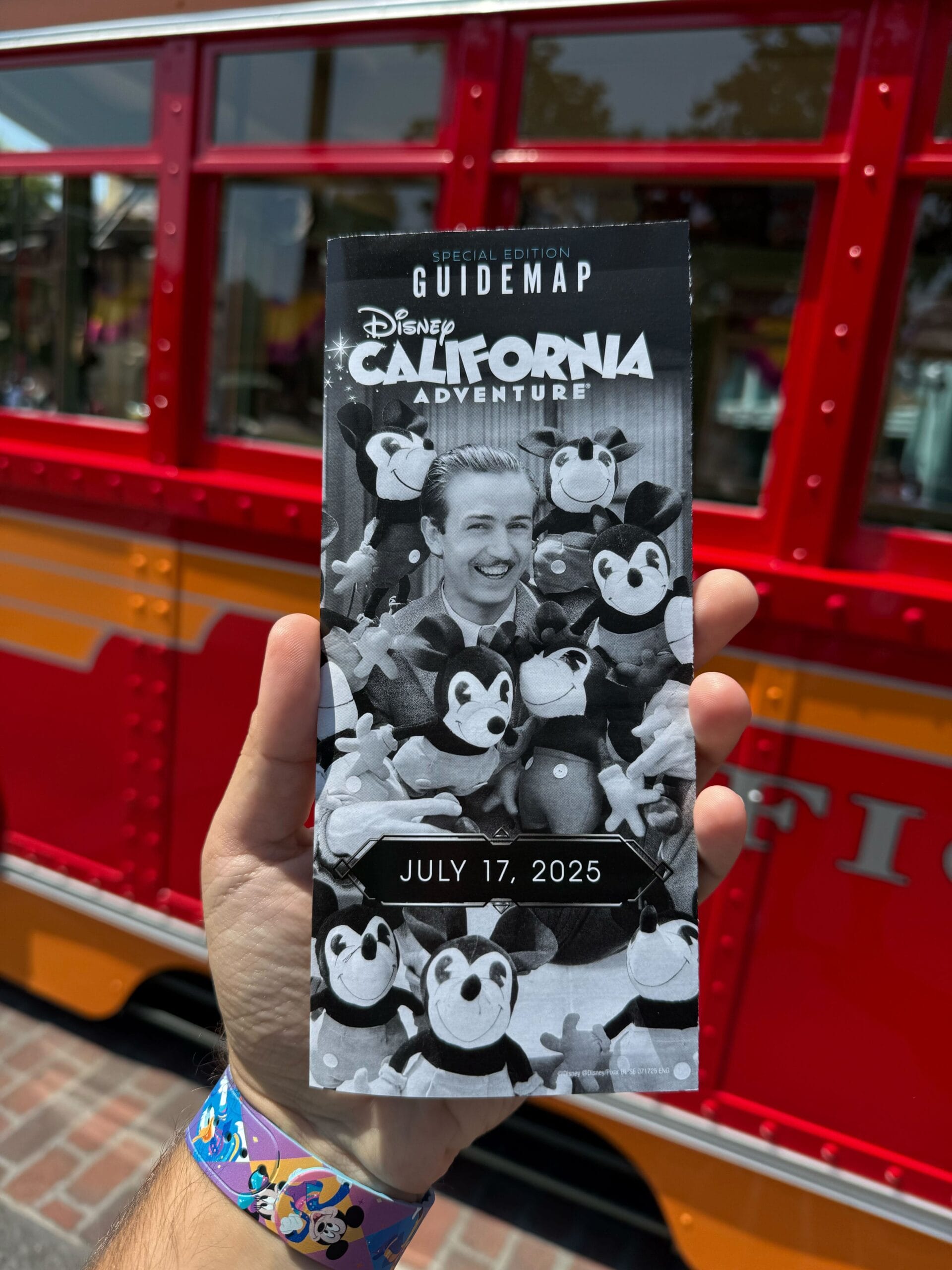 Hand holding a Disney California Adventure guidemap dated July 17, 2025, in front of a red trolley.