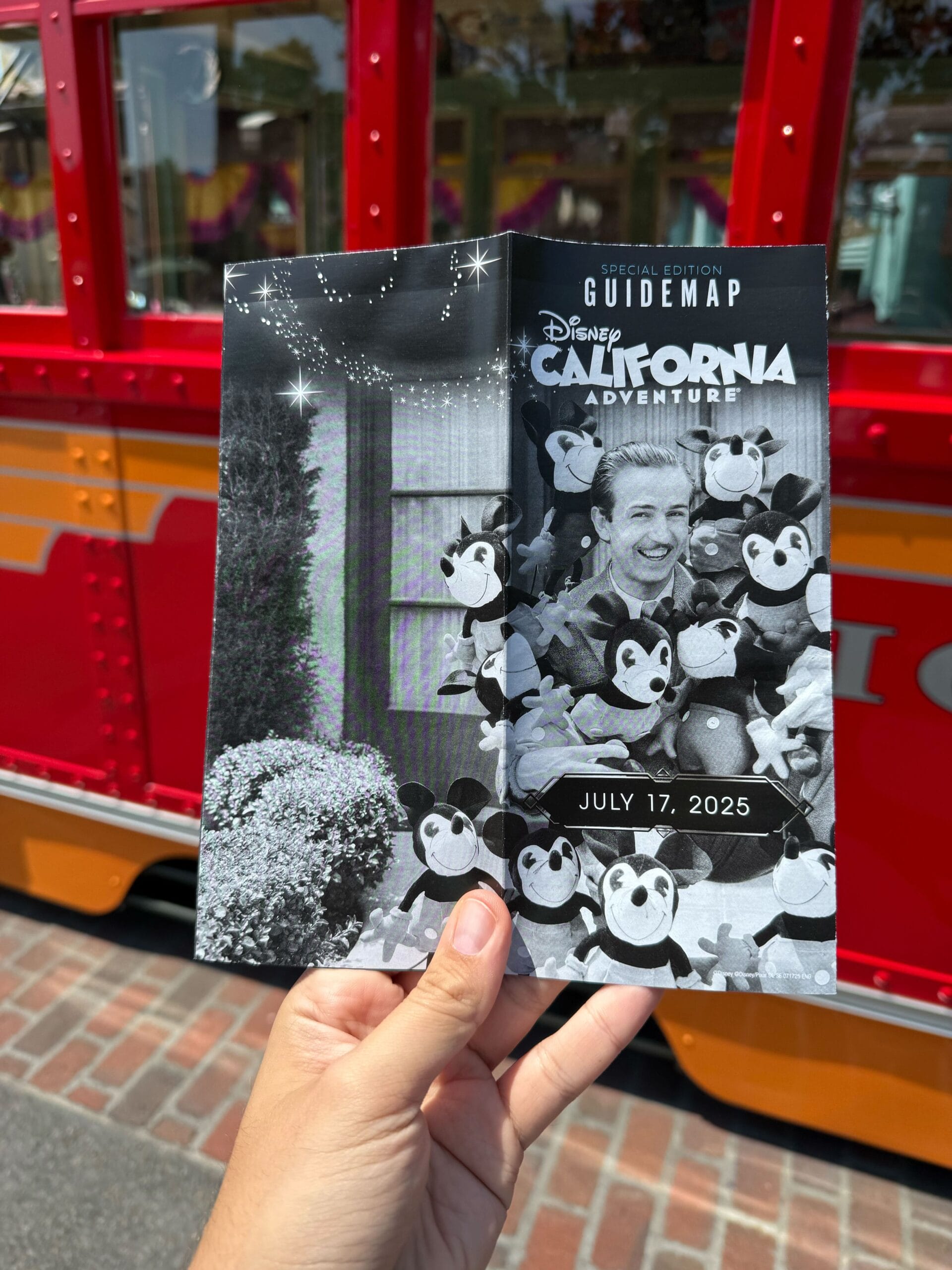 A hand holds a Disney California Adventure guide map dated July 17, 2025, in front of a red trolley.