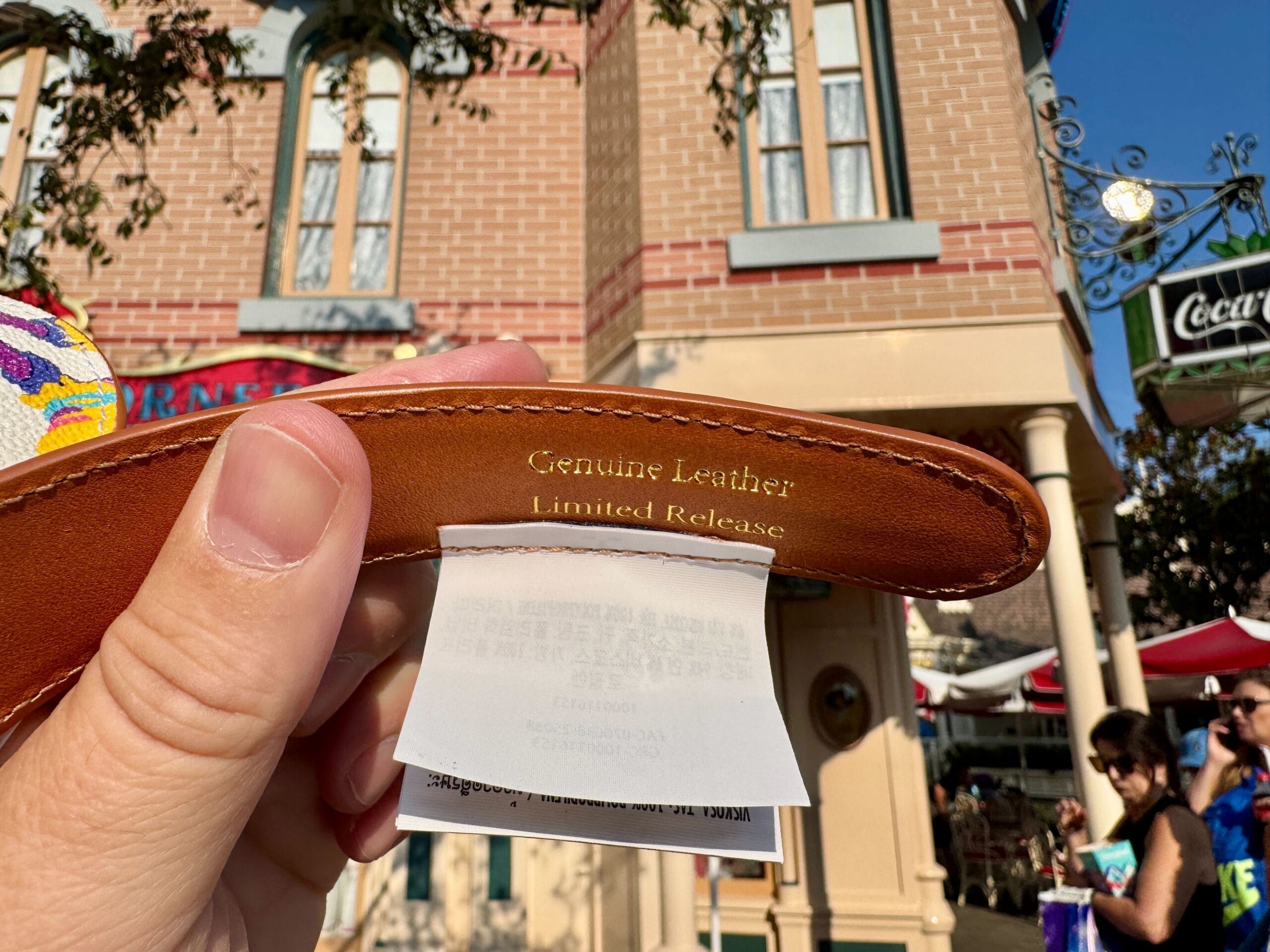 A hand holds a leather strap labeled "Genuine Leather Limited Release," exclusive Disneyland 70th Anniversary merchandise.