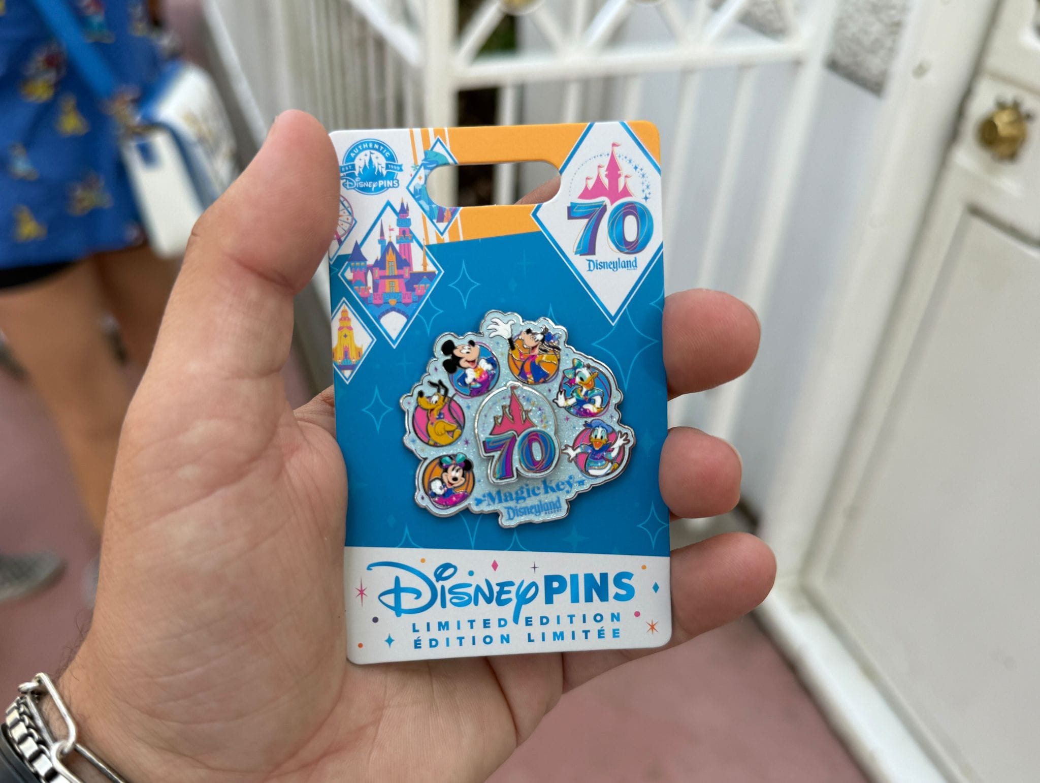 Hand holding a Disneyland 70th Anniversary collectible pin, released on July 17, featuring Mickey and friends.