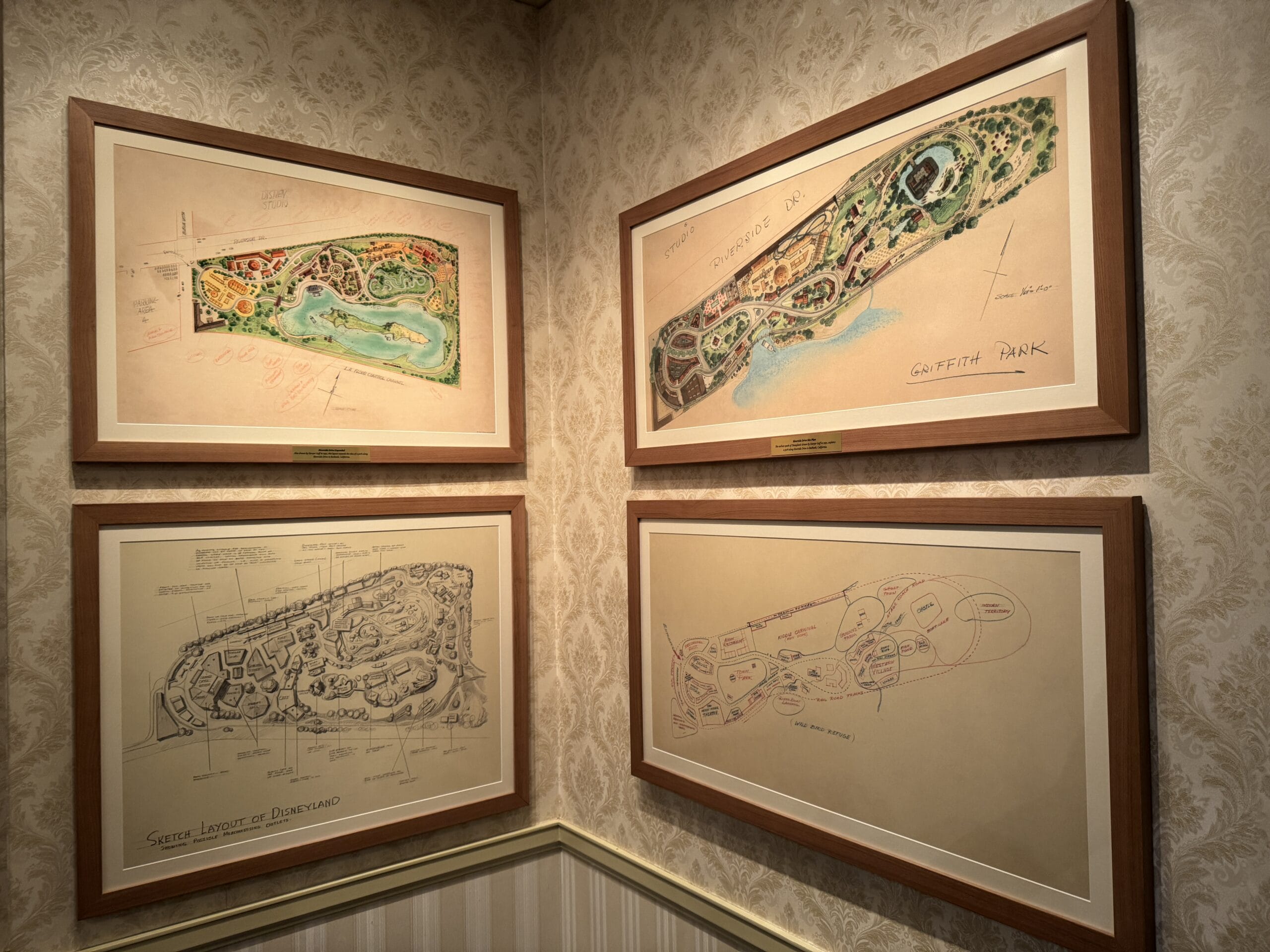 Four framed sketches and maps, like photo exhibits, displayed on a wallpapered corner wall of Main Street Opera House.