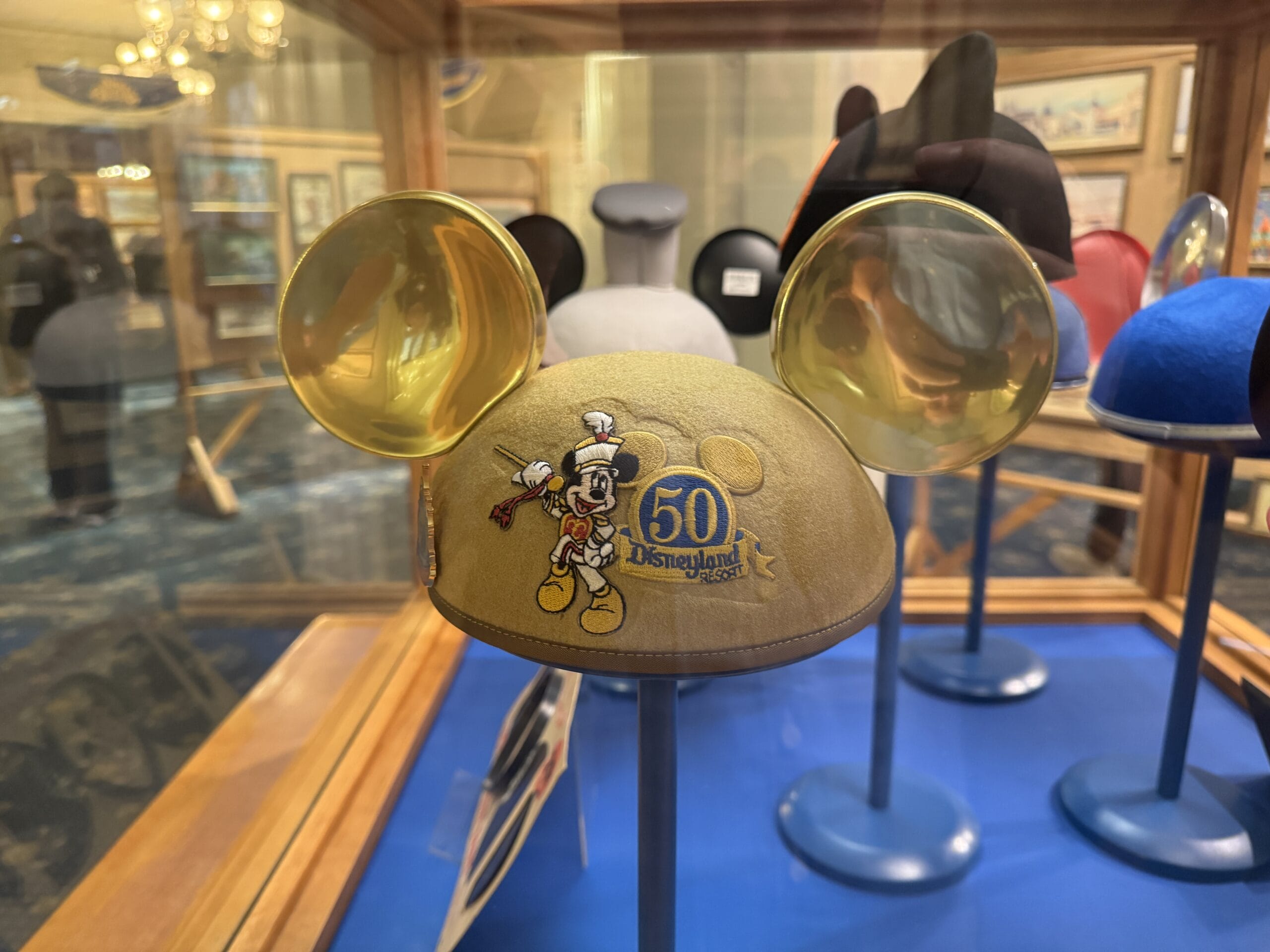 Gold Mickey Mouse ears hat with 50th Disneyland logo, featured in new exhibits at Main Street Opera House; photos show other hats.