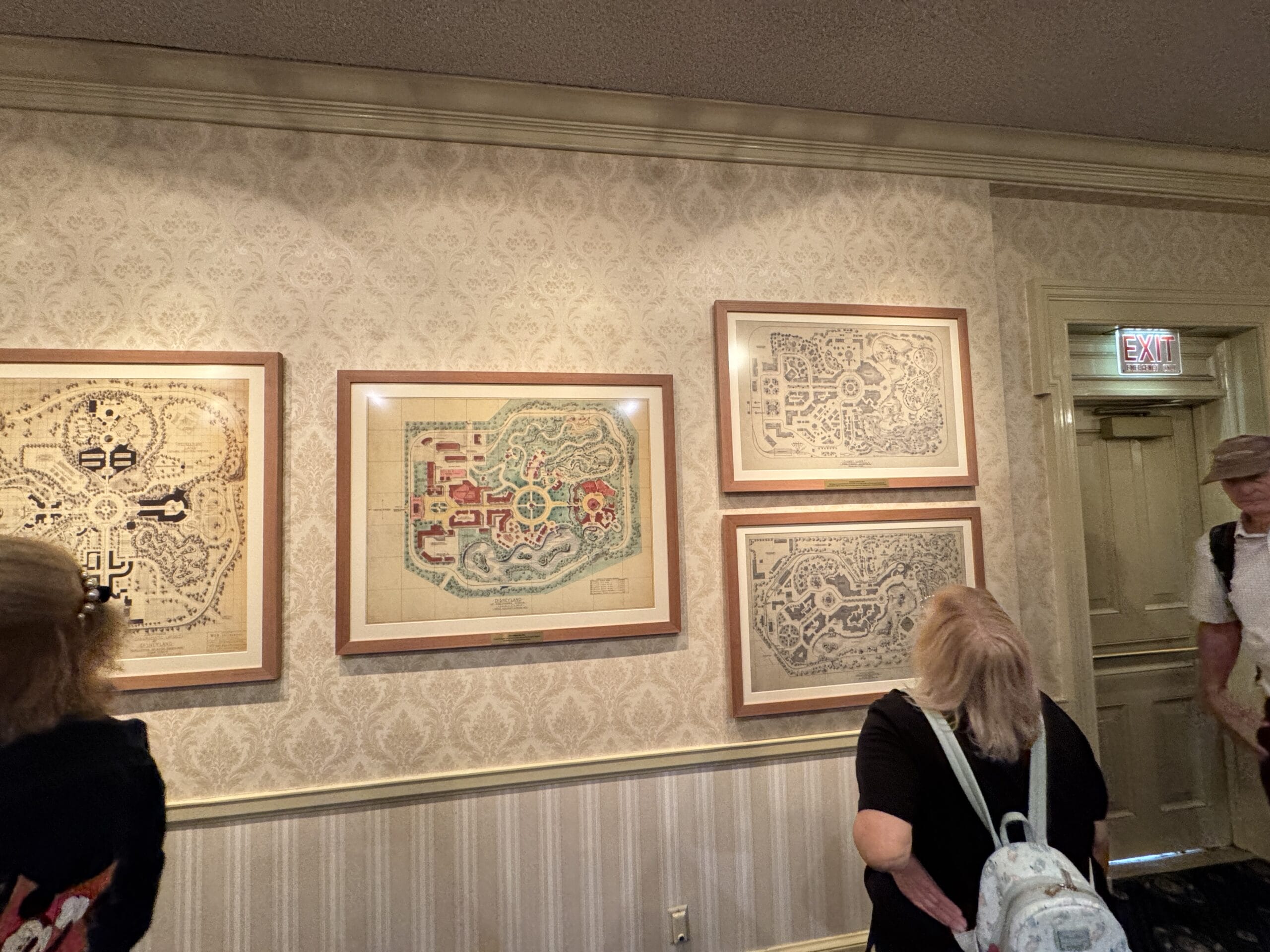 Three people view framed vintage park maps and photos at the Main Street Opera House’s new exhibits in a softly lit room.