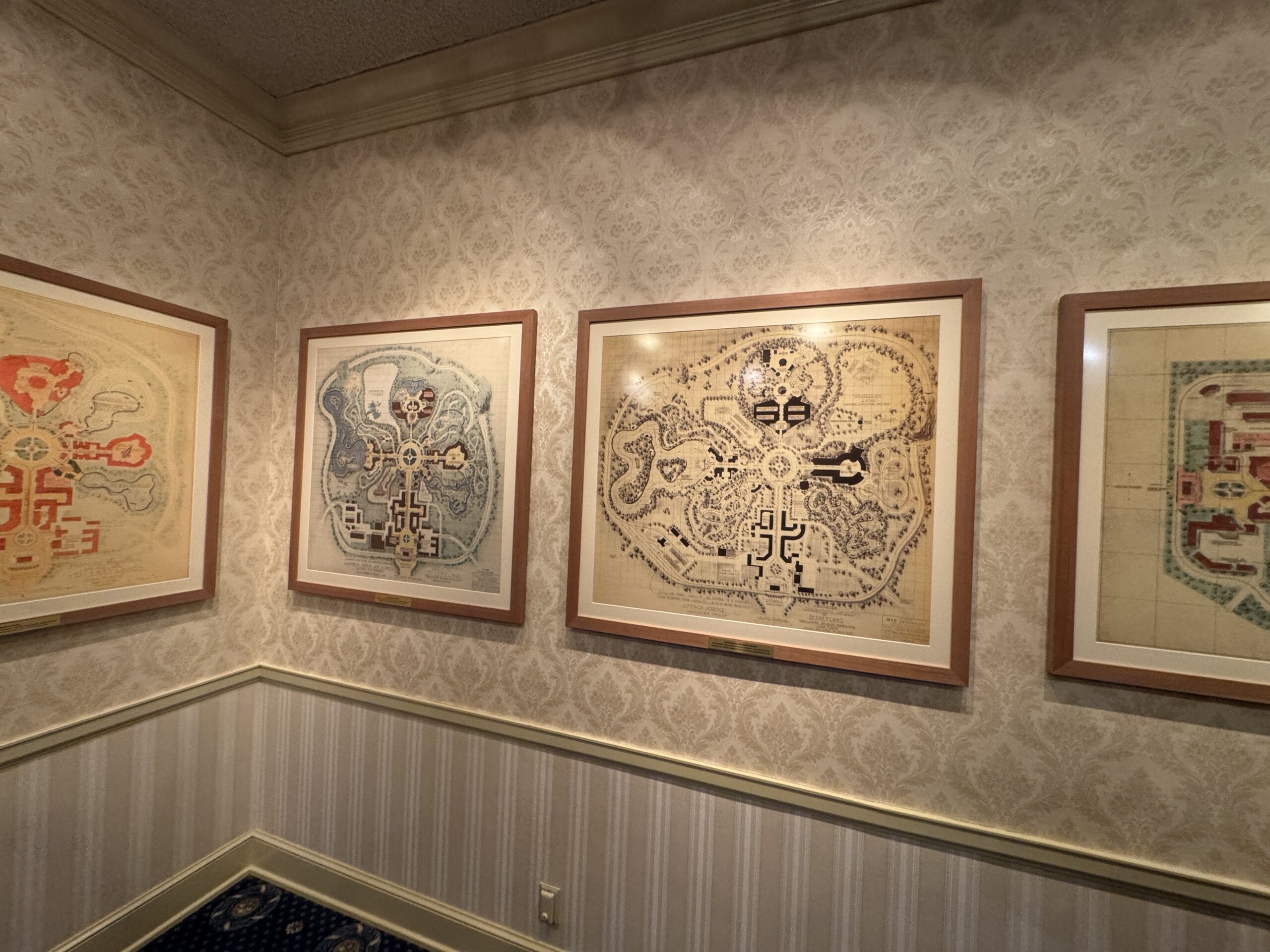 Framed vintage theme park maps and photos hang on a wallpapered wall, reminiscent of Main Street Opera House charm.
