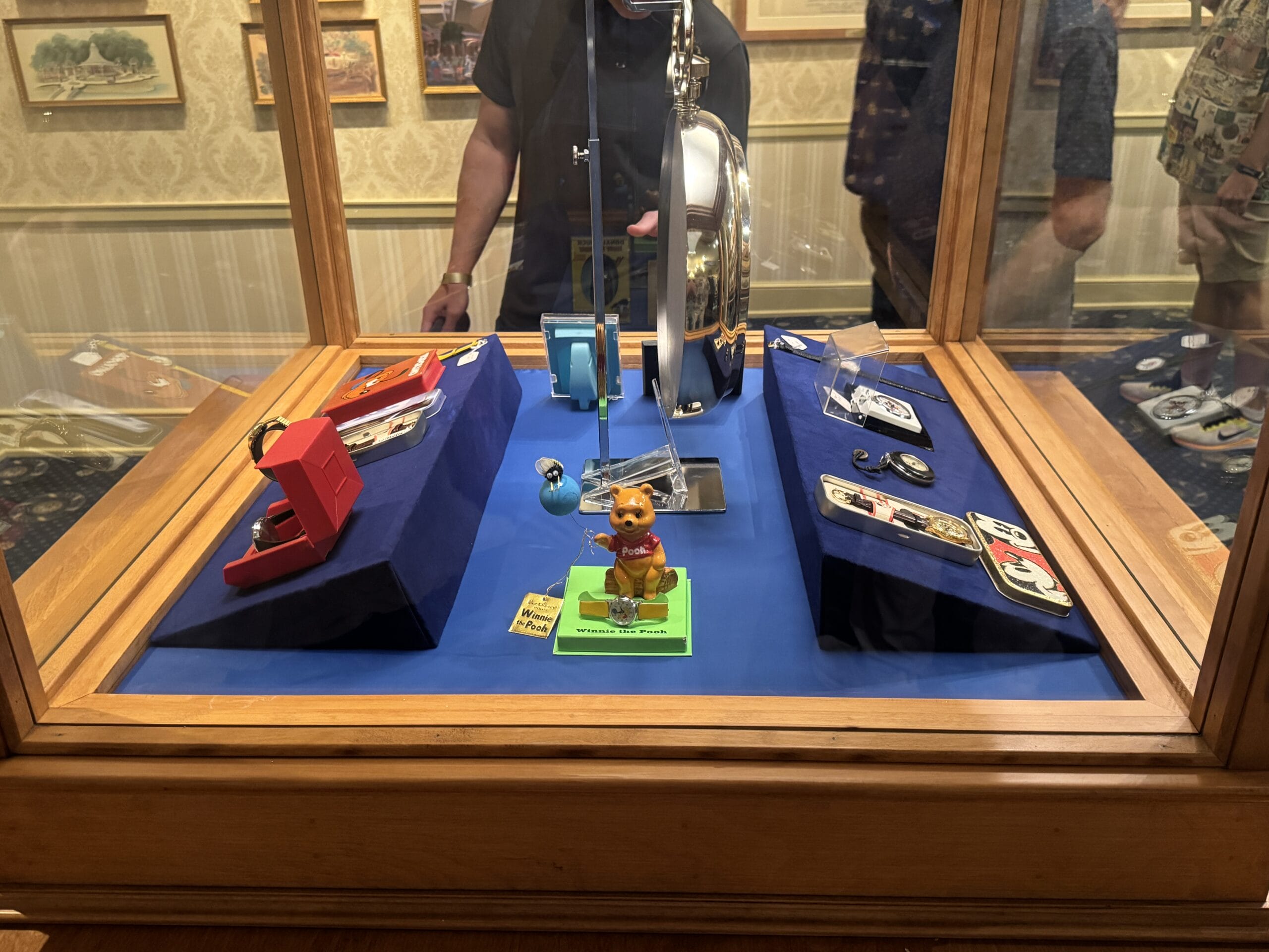 Display case at Main Street Opera House with vintage gadgets, cat figurine, and reflection of people viewing new exhibits.