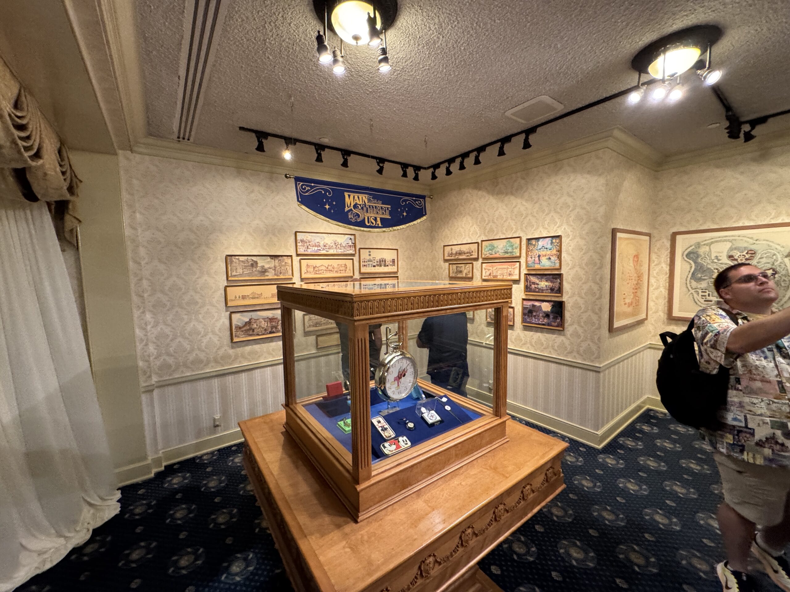 A display case with collectibles in a museum room, featuring photos and framed pictures on patterned walls.