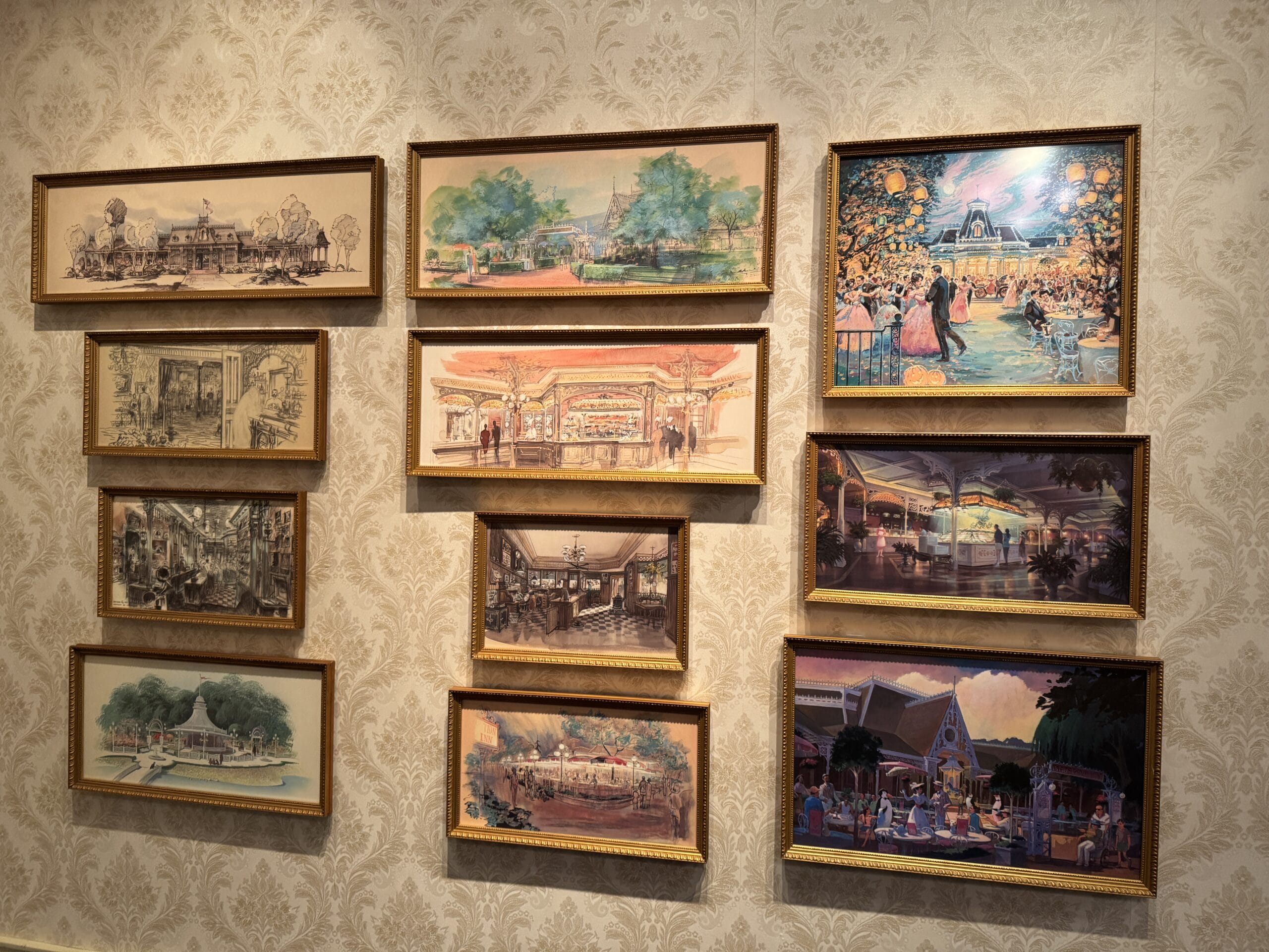 Nine framed concept art photos of buildings and parks hang on a patterned wallpapered wall at Main Street Opera House.