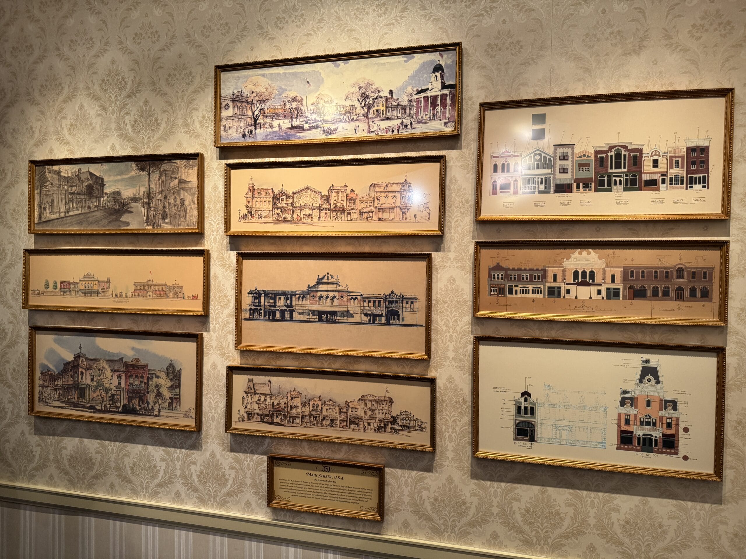 Framed architectural sketches and photos of buildings hang in a grid on a patterned wallpapered wall.