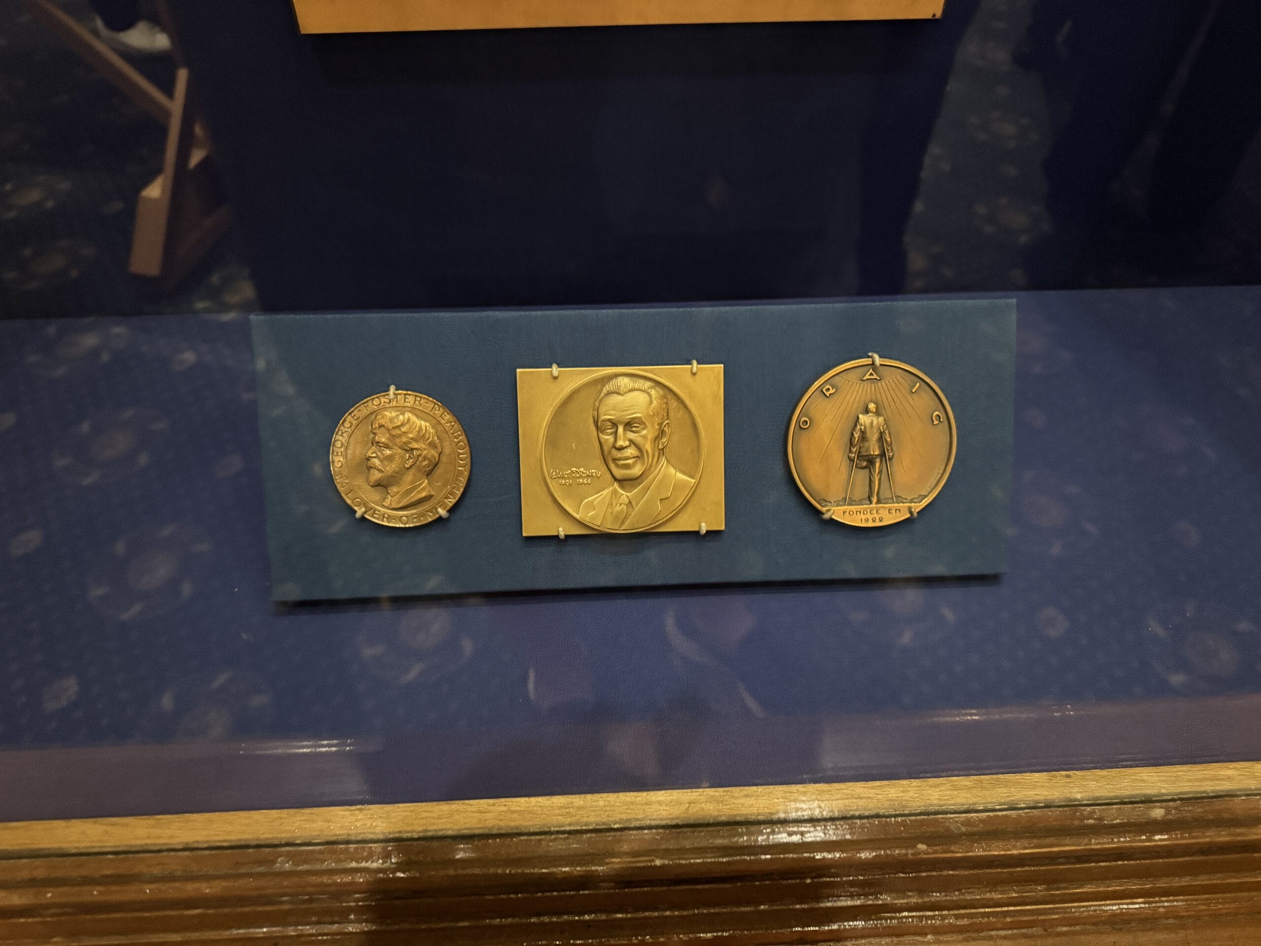 Three gold medals displayed in a case at the Main Street Opera House, with engraved portraits and photos of new exhibits.