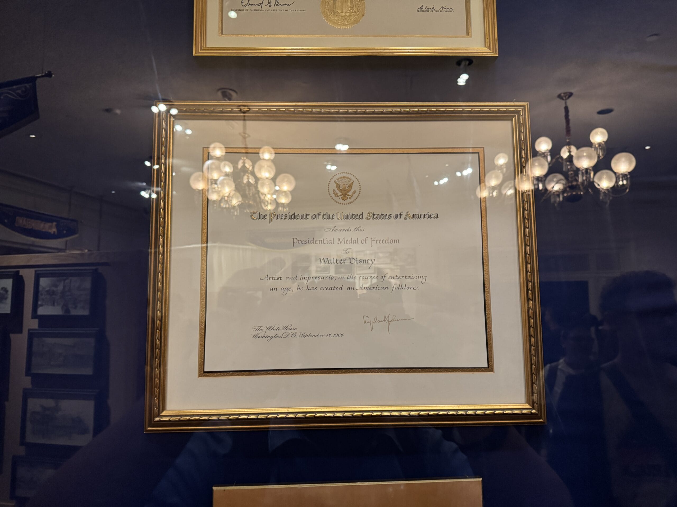 A framed Presidential Medal of Freedom certificate on display at the Main Street Opera House, reflections and photos visible.