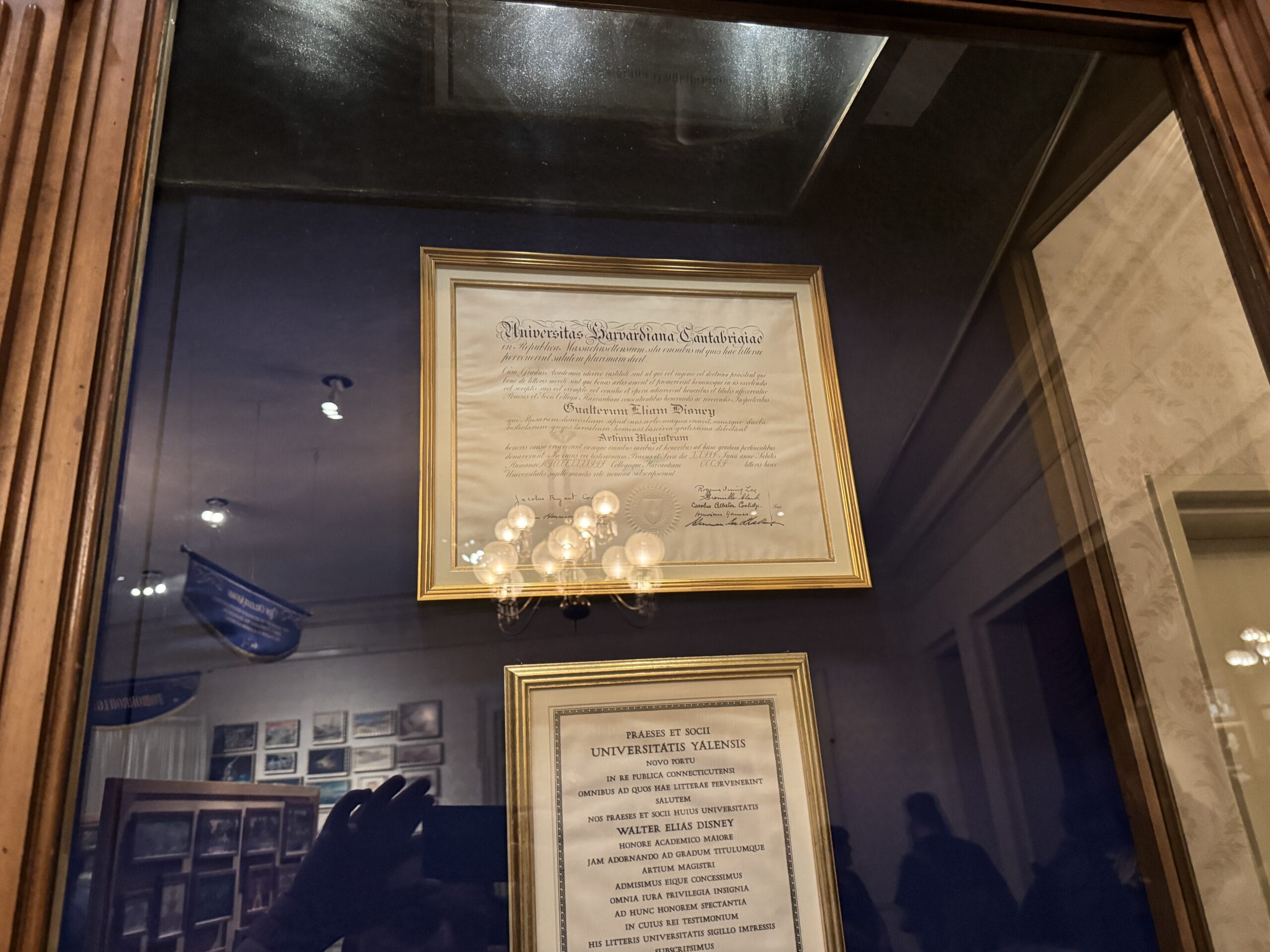 A framed diploma and certificate behind glass, reflecting a chandelier—photos from Main Street Opera House's new exhibits.