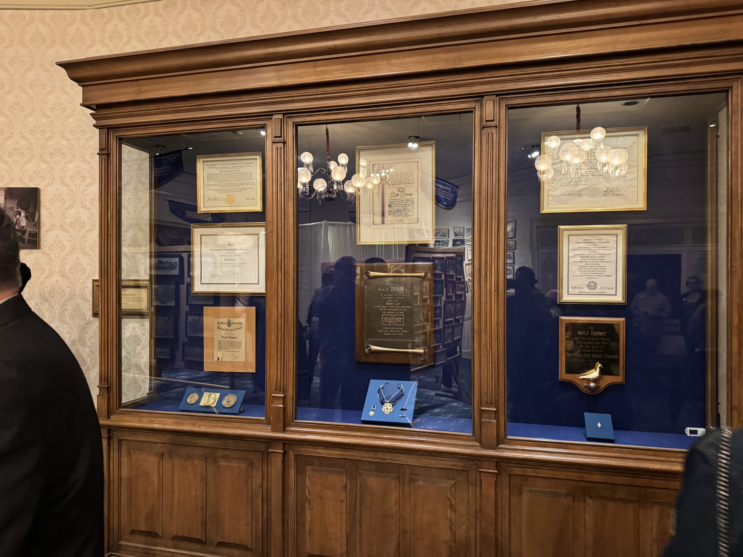 A wooden display case holds plaques, framed documents, and medals in the Main Street Opera House’s museum setting.