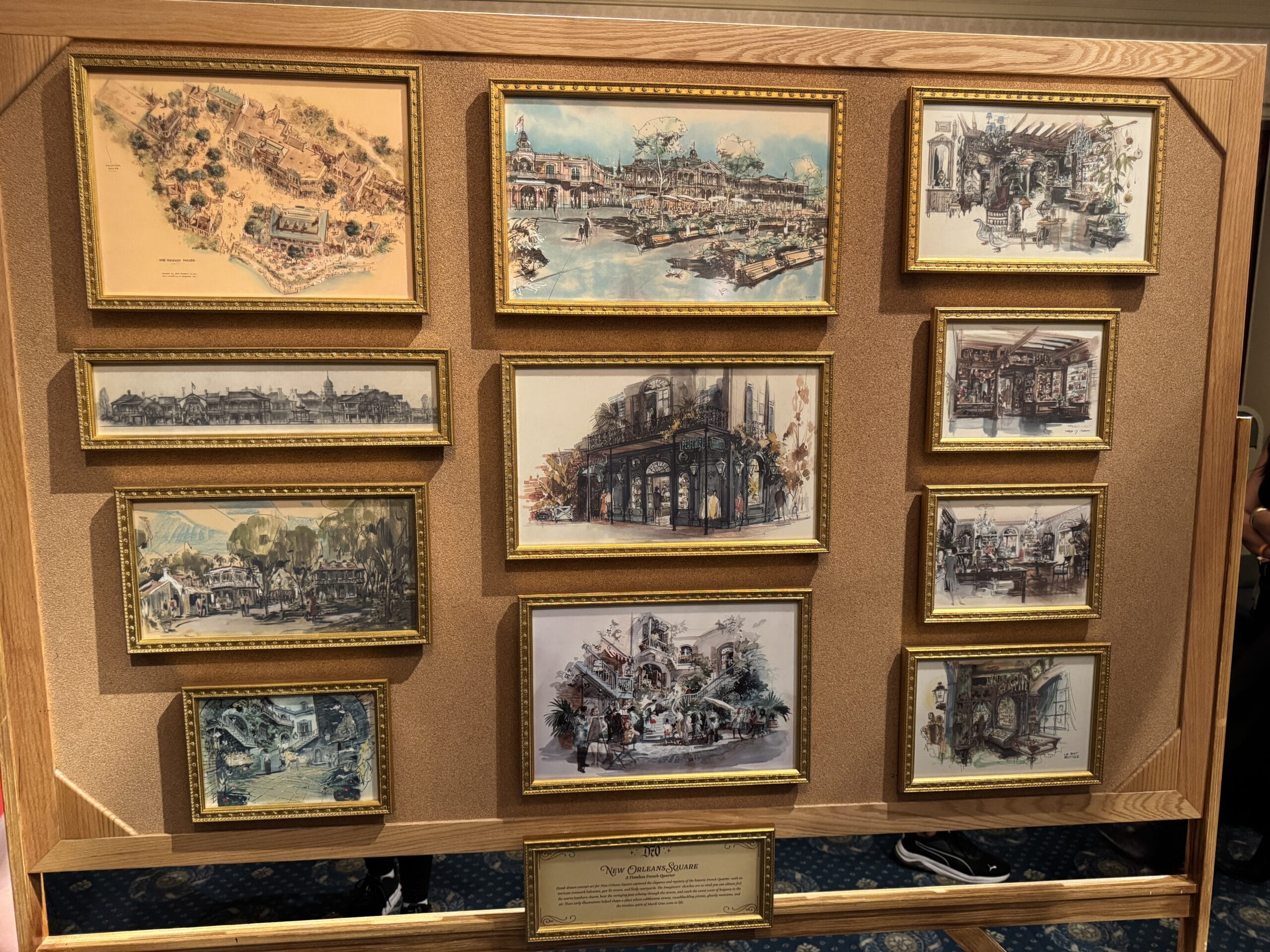 A display board with framed vintage-style illustrations of Main Street Opera House and Disneyland history in a wooden frame.