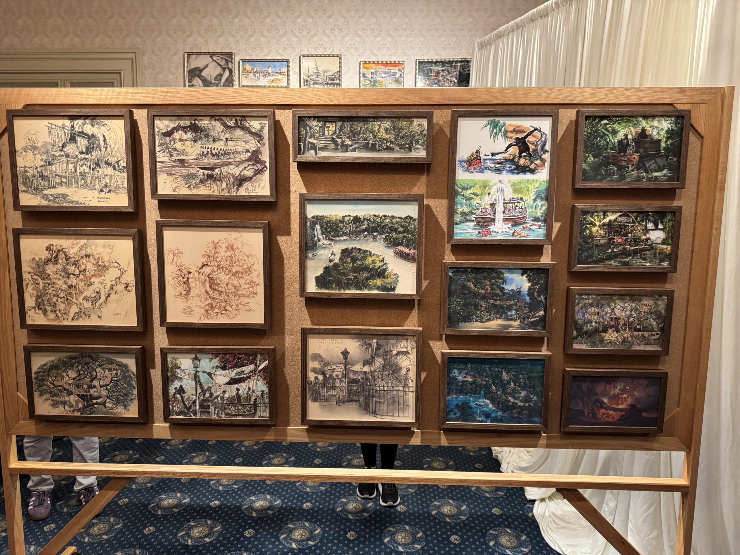A wooden display holds sketches of jungle adventures, echoing Disneyland history, in a carpeted room.