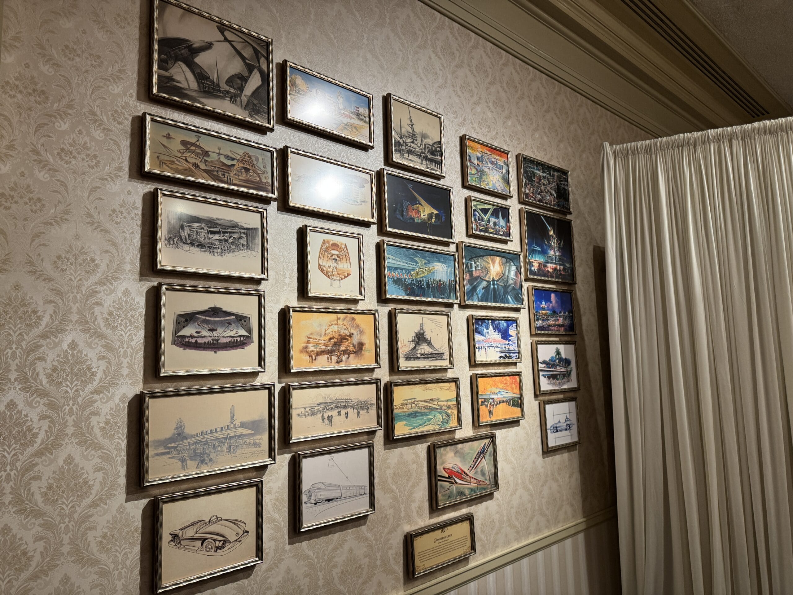 Framed concept art and sketches in a grid recall Main Street Opera House and Disneyland history by a white curtain.