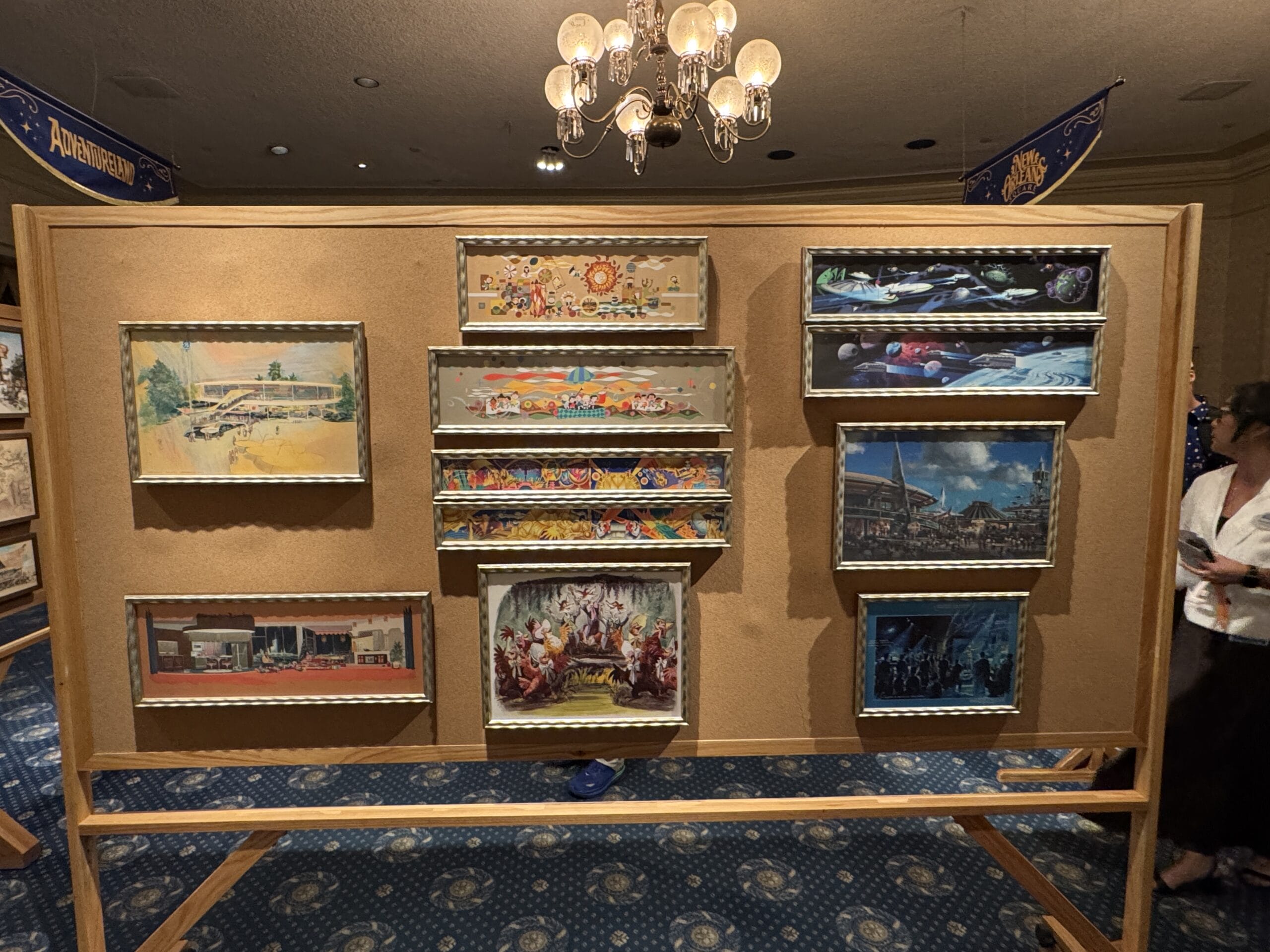 A display board holds nine framed paintings in a room with blue carpet at the Main Street Opera House.