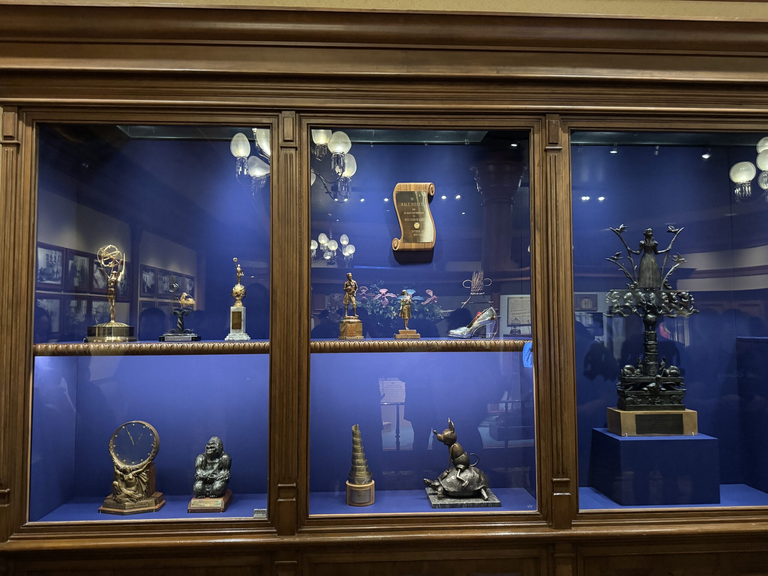 A wooden display case with a blue background at Main Street Opera House holds awards, small statues, and various figurines.