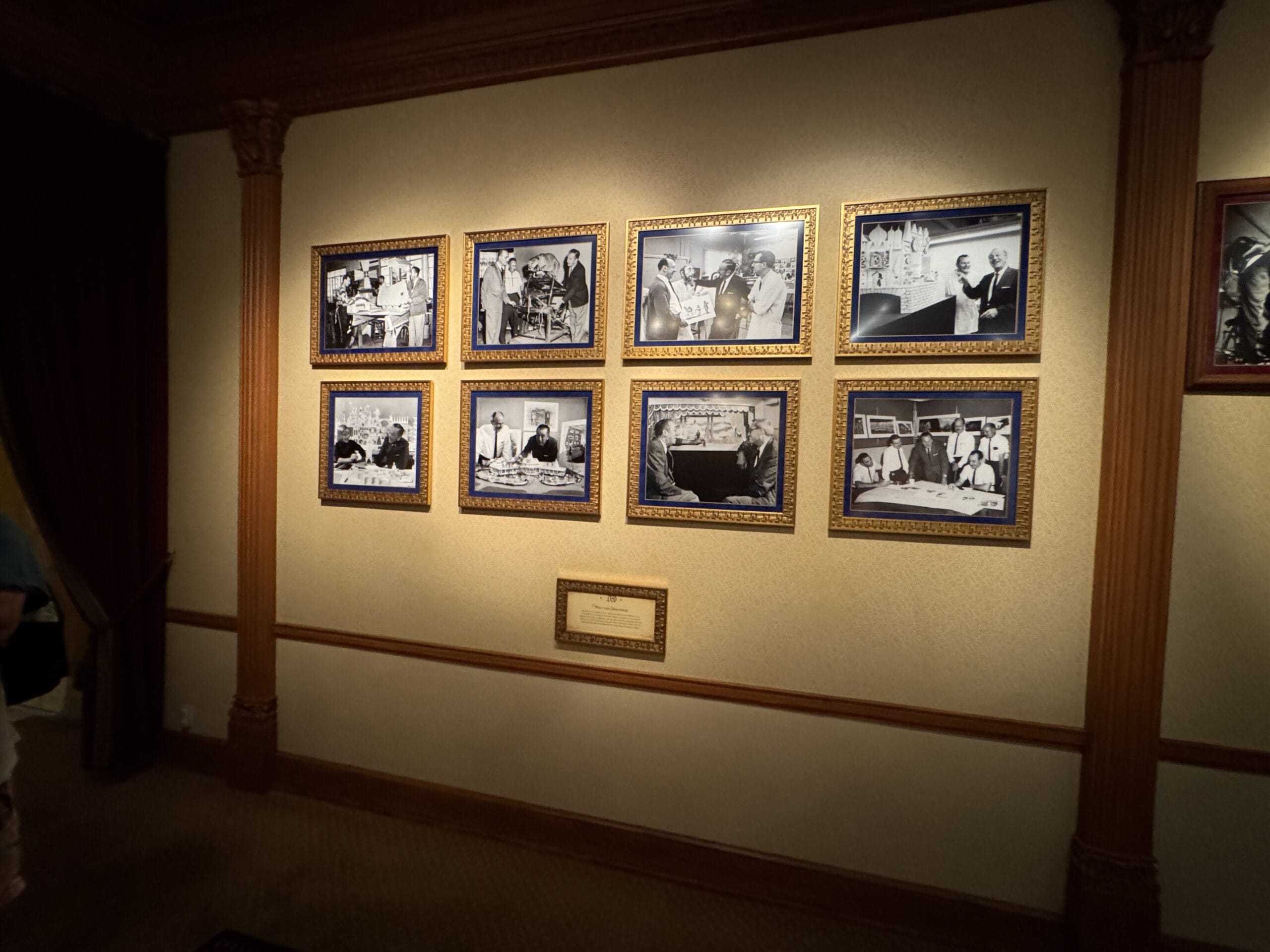 A wall at Main Street Opera House displays nine framed black-and-white photos of people working at desks, with a plaque.