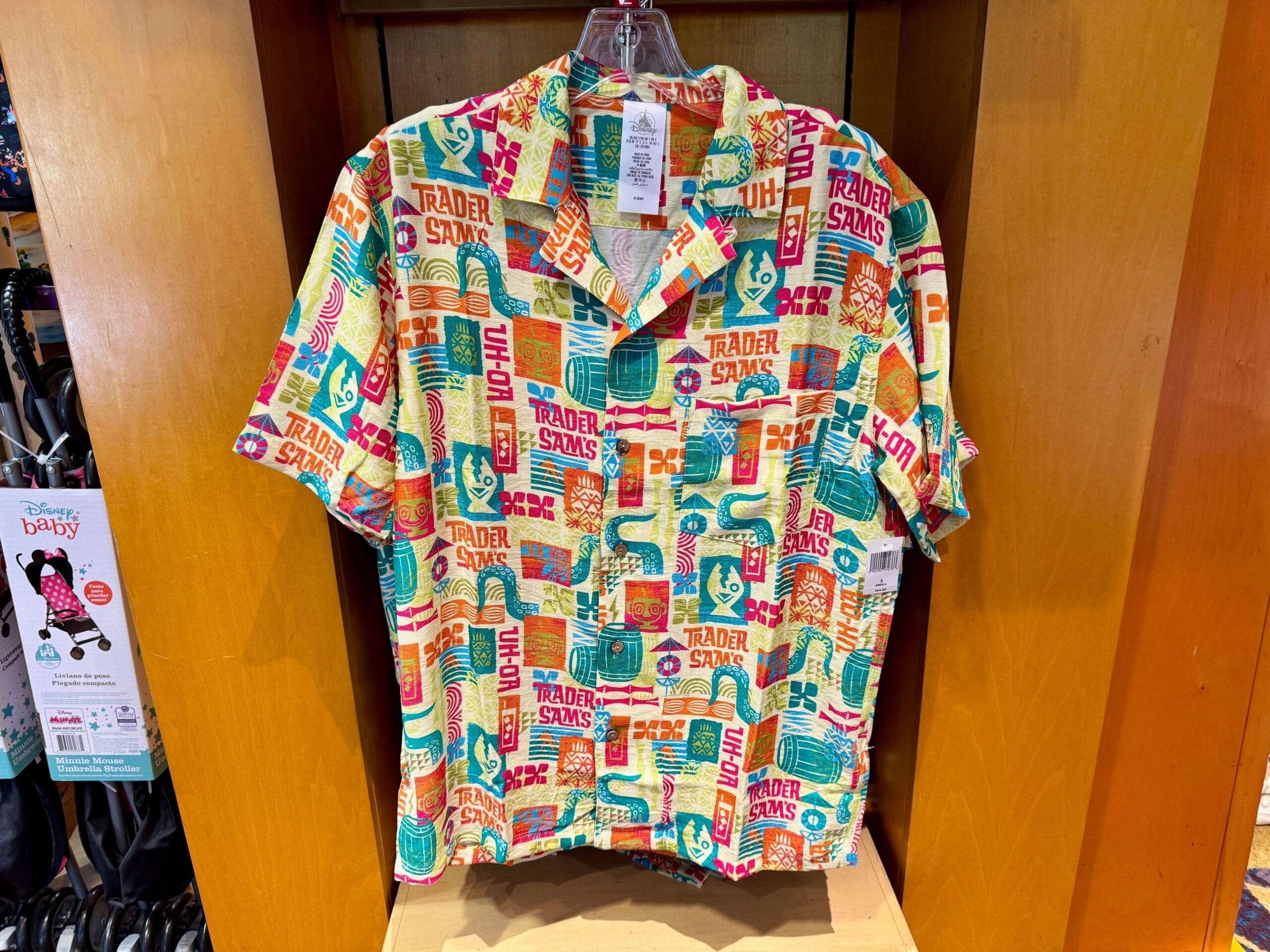 Colorful Trader Sam’s Hawaiian shirt with tropical and tiki-themed patterns, displayed on a wooden shelf.