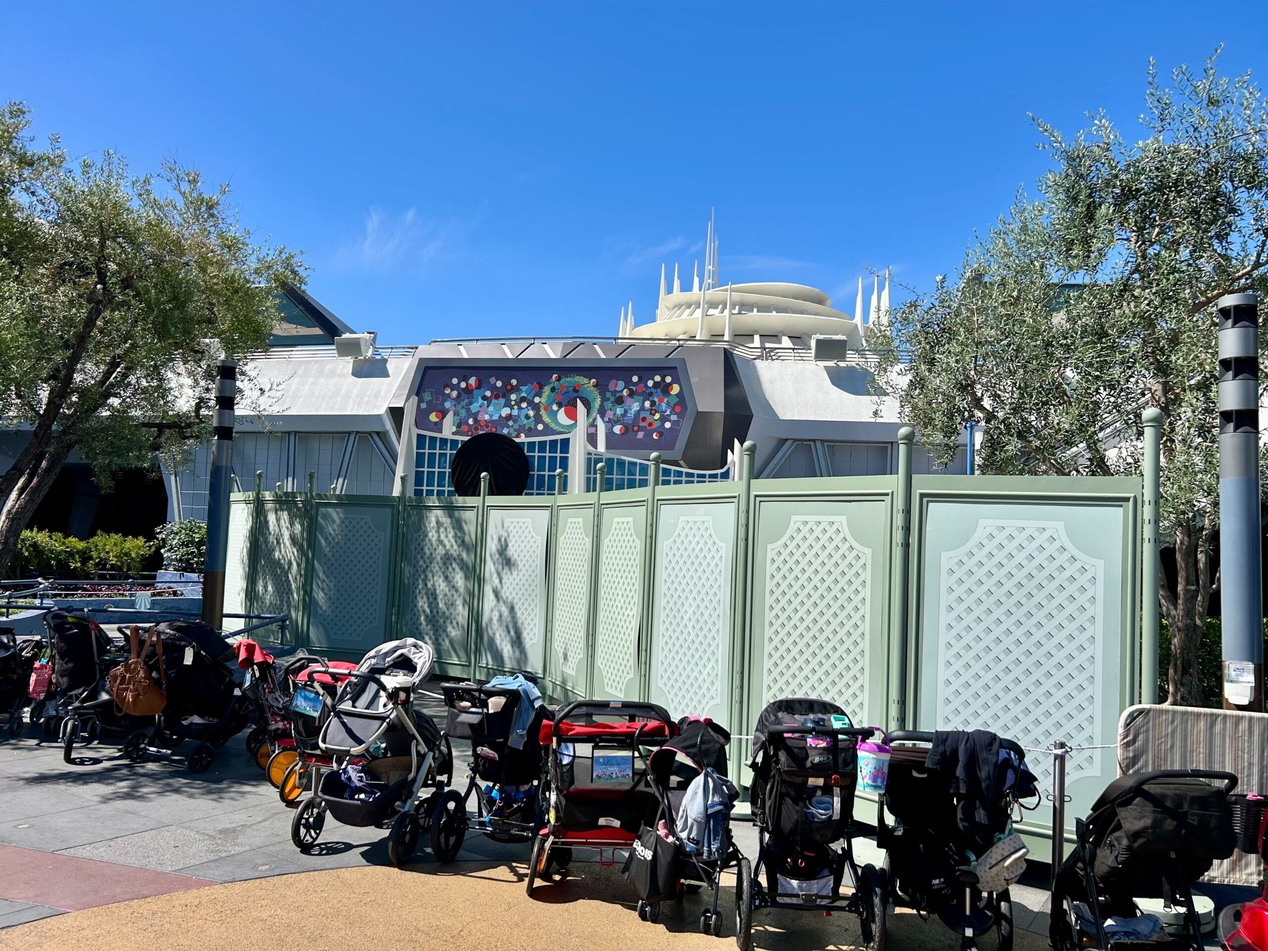 Strollers lined up in front of construction walls at Disneyland Park under a clear blue sky, ready for a meet and greet.