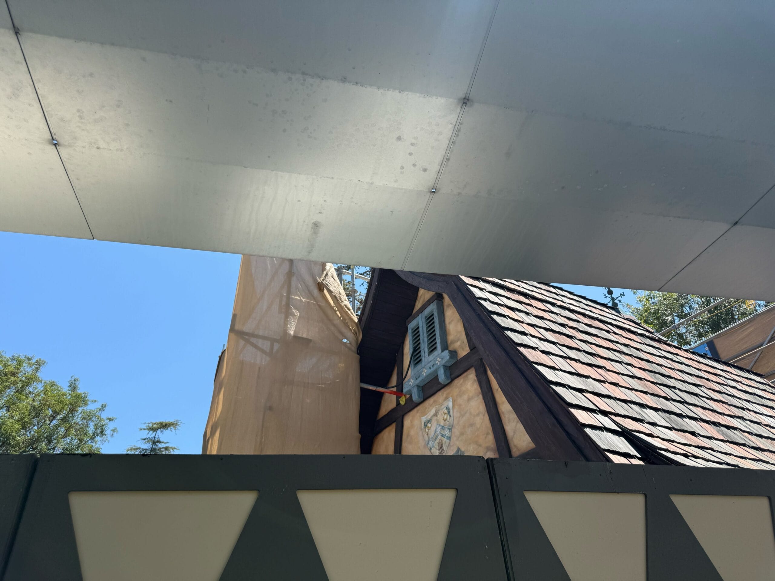 A-frame roof and dormer window of new construction, partially hidden by a barrier and tarp.