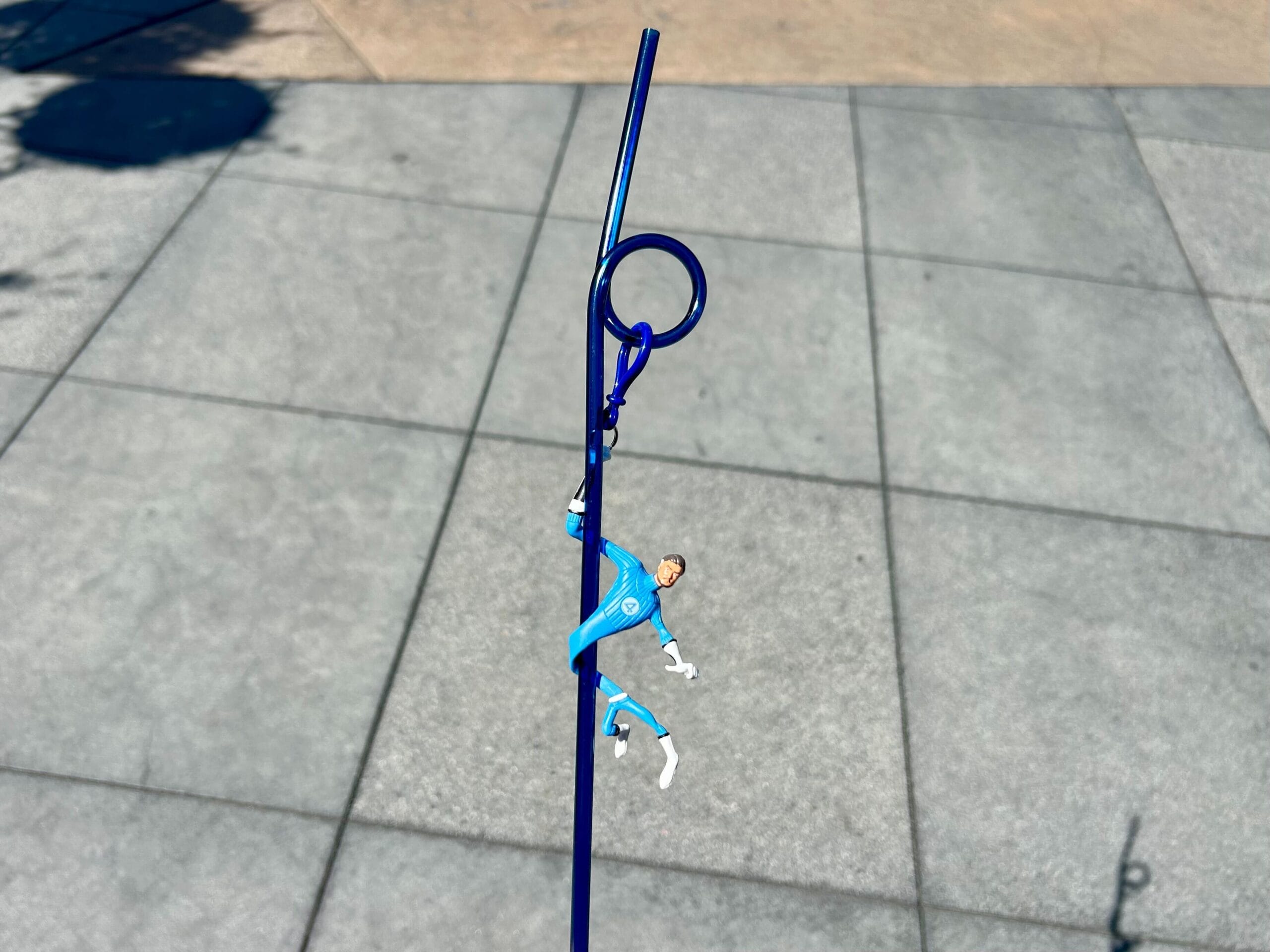 A small toy soccer player hanging from a blue straw on a tiled outdoor surface.