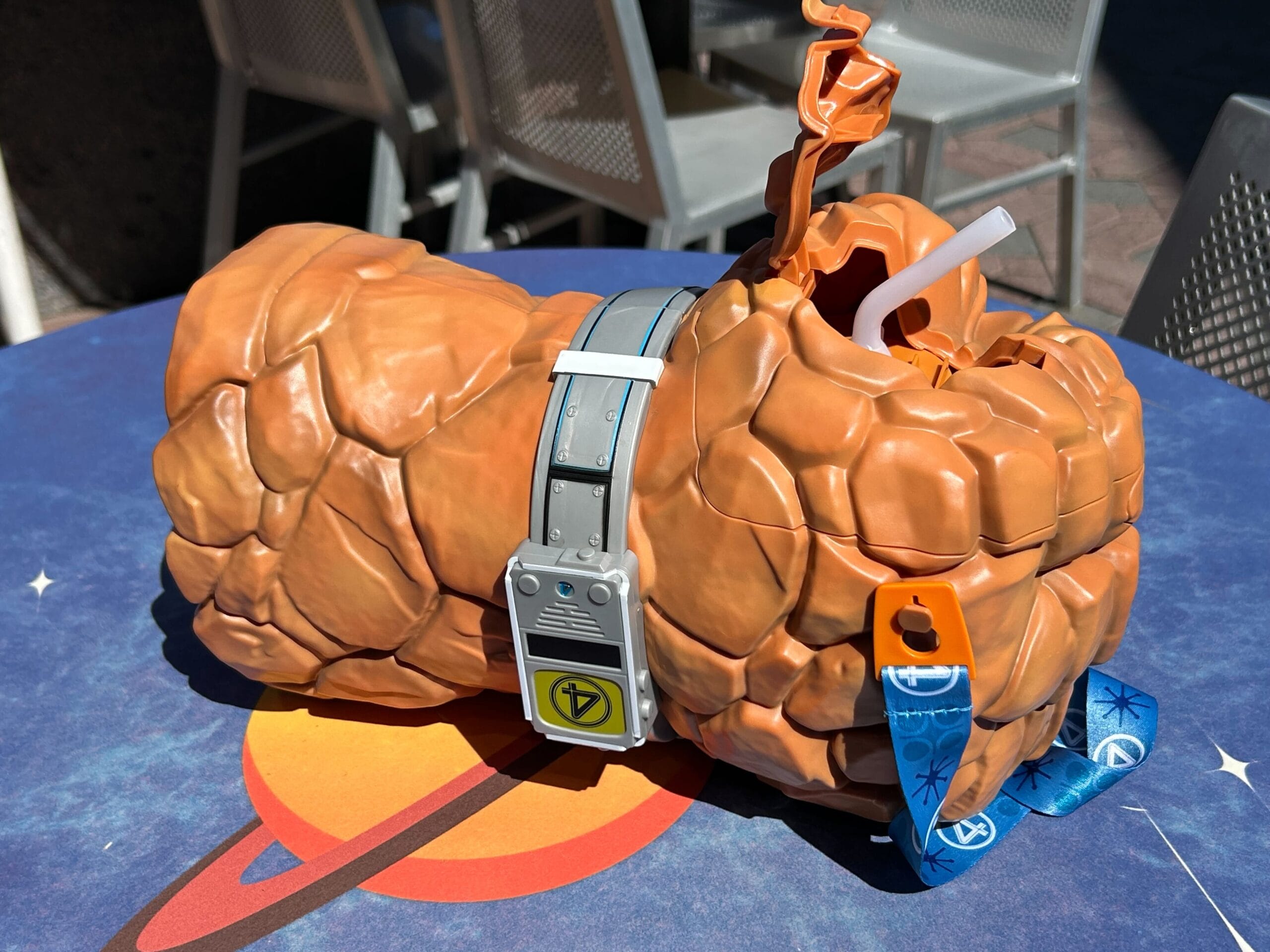 A drink cup shaped like The Thing’s rocky orange arm sits on a blue table with a space design.
