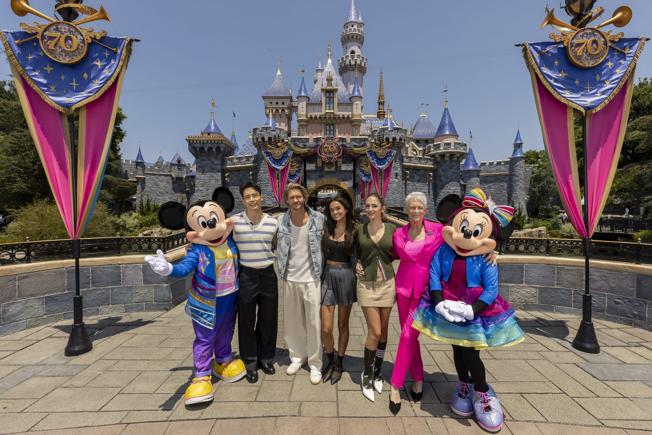 The Freaky Friday cast poses with Mickey and Minnie in front of Disneyland's banner-adorned Sleeping Beauty Castle.