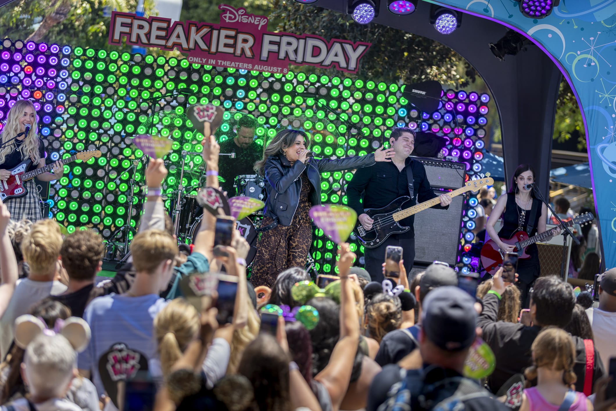 A band performs on an outdoor stage at Disneyland under a "Freaky Friday" Disney sign with colorful lights.