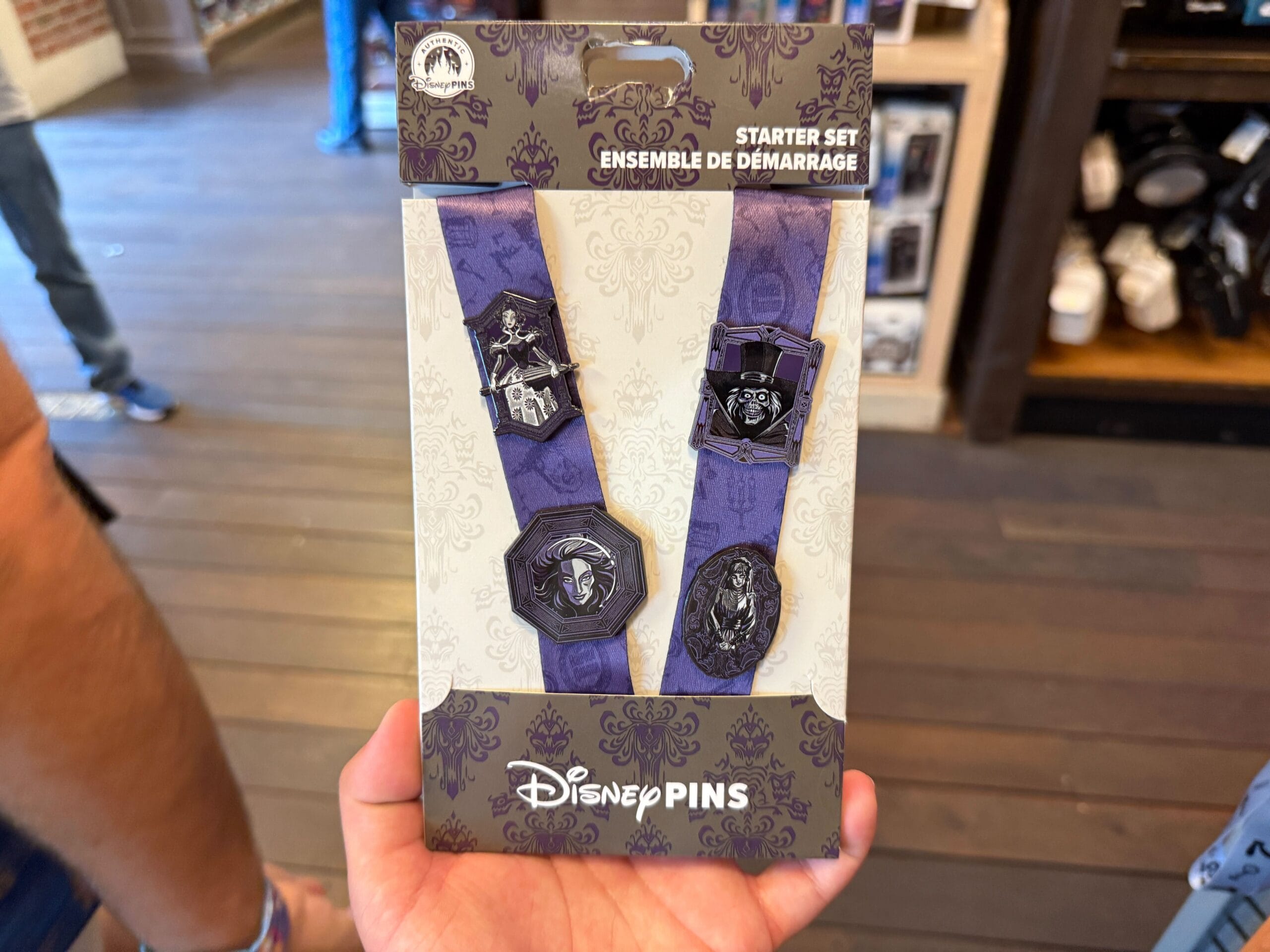 A hand holds a Haunted Mansion starter pin set in front of a store display.