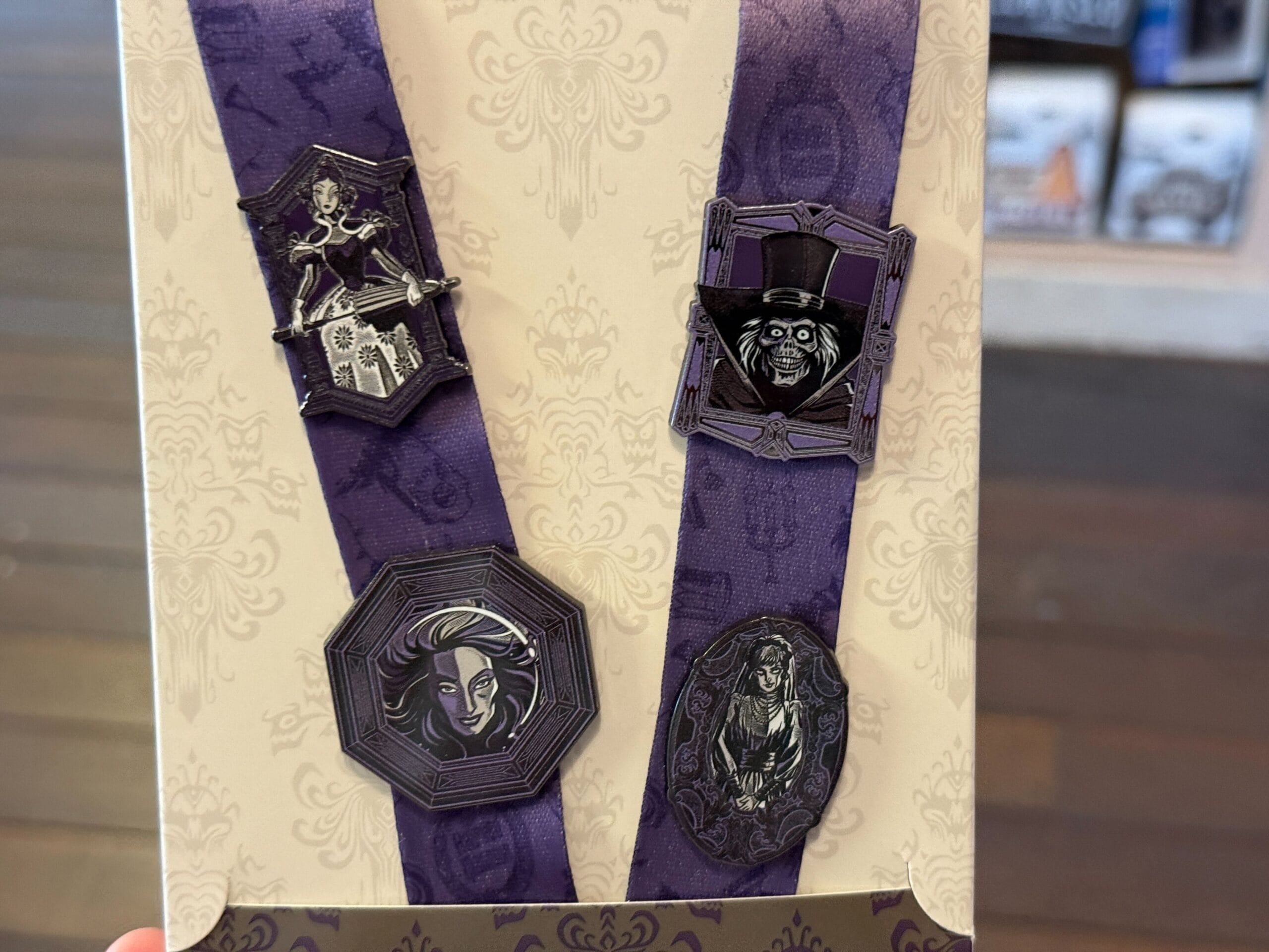 Four haunted mansion-themed pins on a purple ribbon, featuring spooky characters and ornate frames.