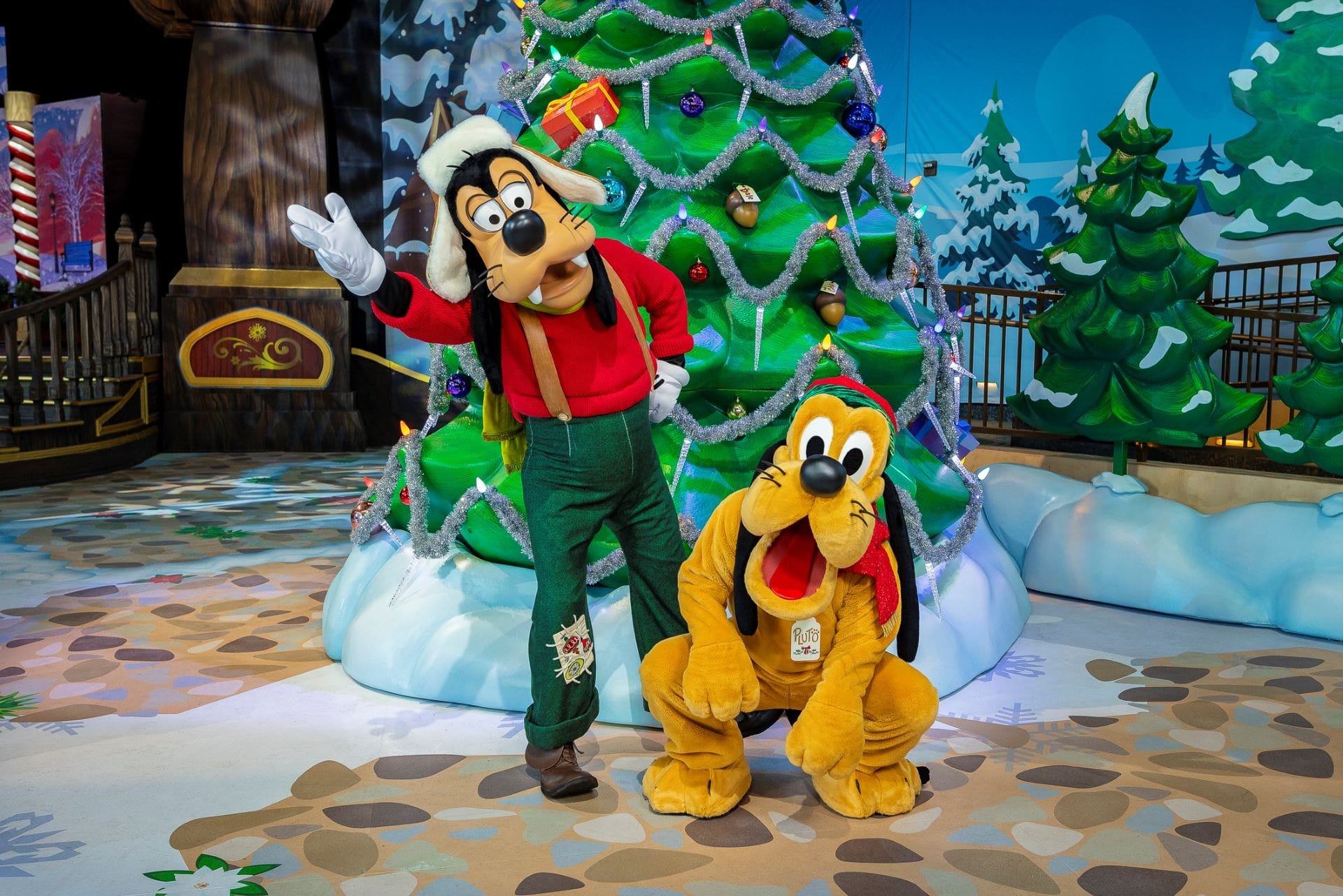 Goofy and Pluto in festive clothes pose at Disneyland Resort before a decorated tree during the 2025 Holidays.
