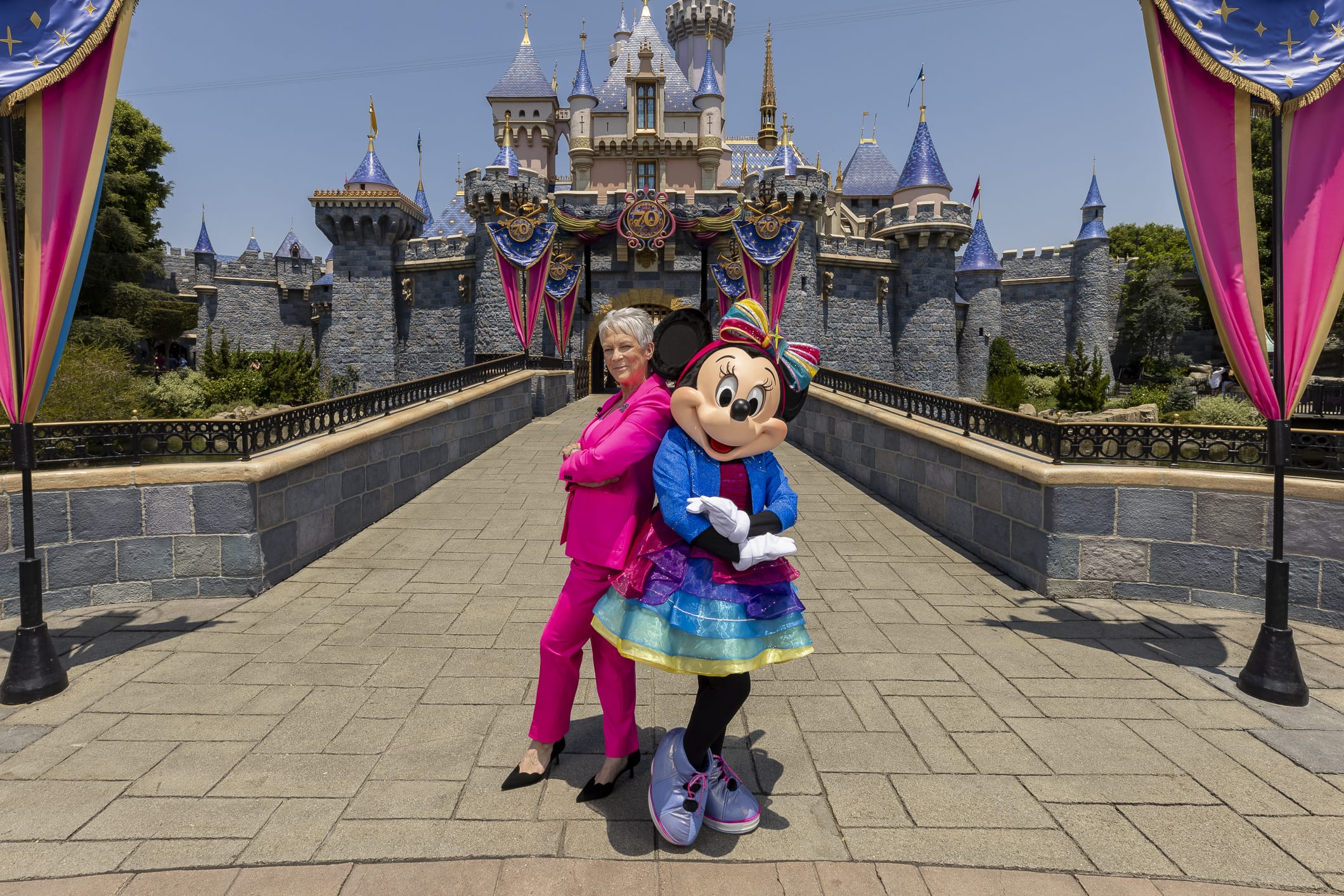 A woman in a pink suit and Minnie Mouse pose back-to-back at Disneyland, like the Freaky Friday cast.